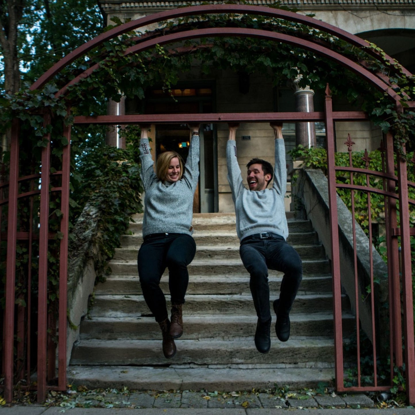 Two people jumping in the air under a decorative archway with greenery.