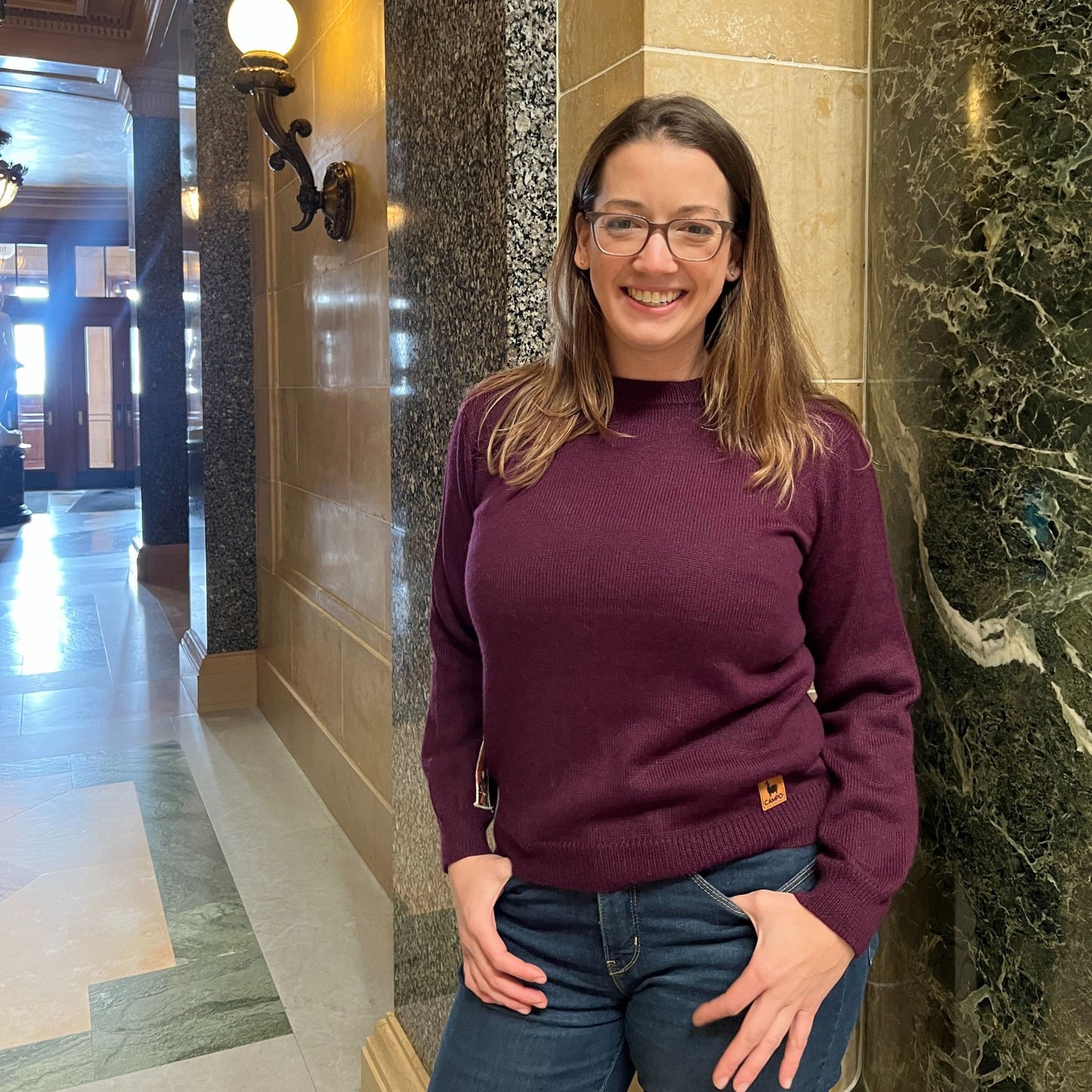 Woman wearing a purple sweater and glasses standing in a marble hallway