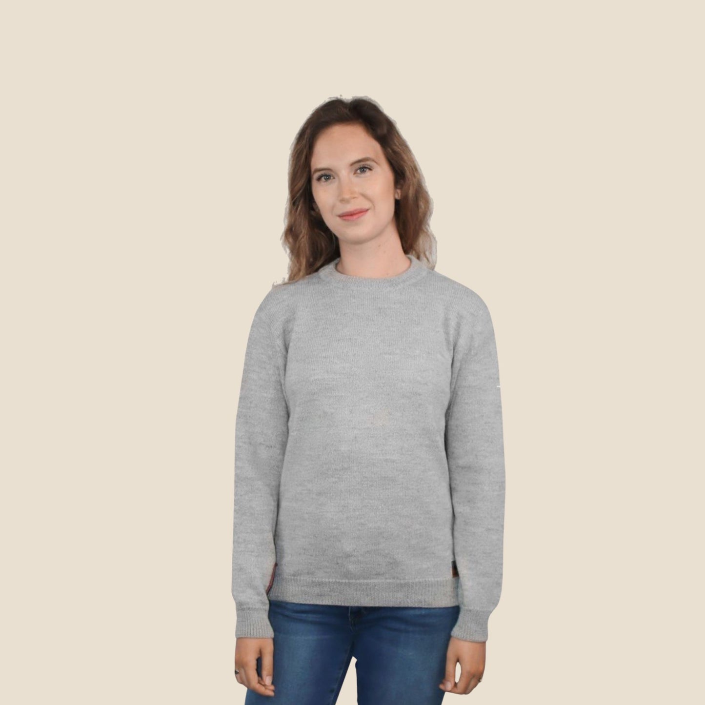 Woman wearing a light gray sweater and blue jeans on a beige background