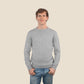 Man wearing a light gray sweater and blue jeans against a beige background