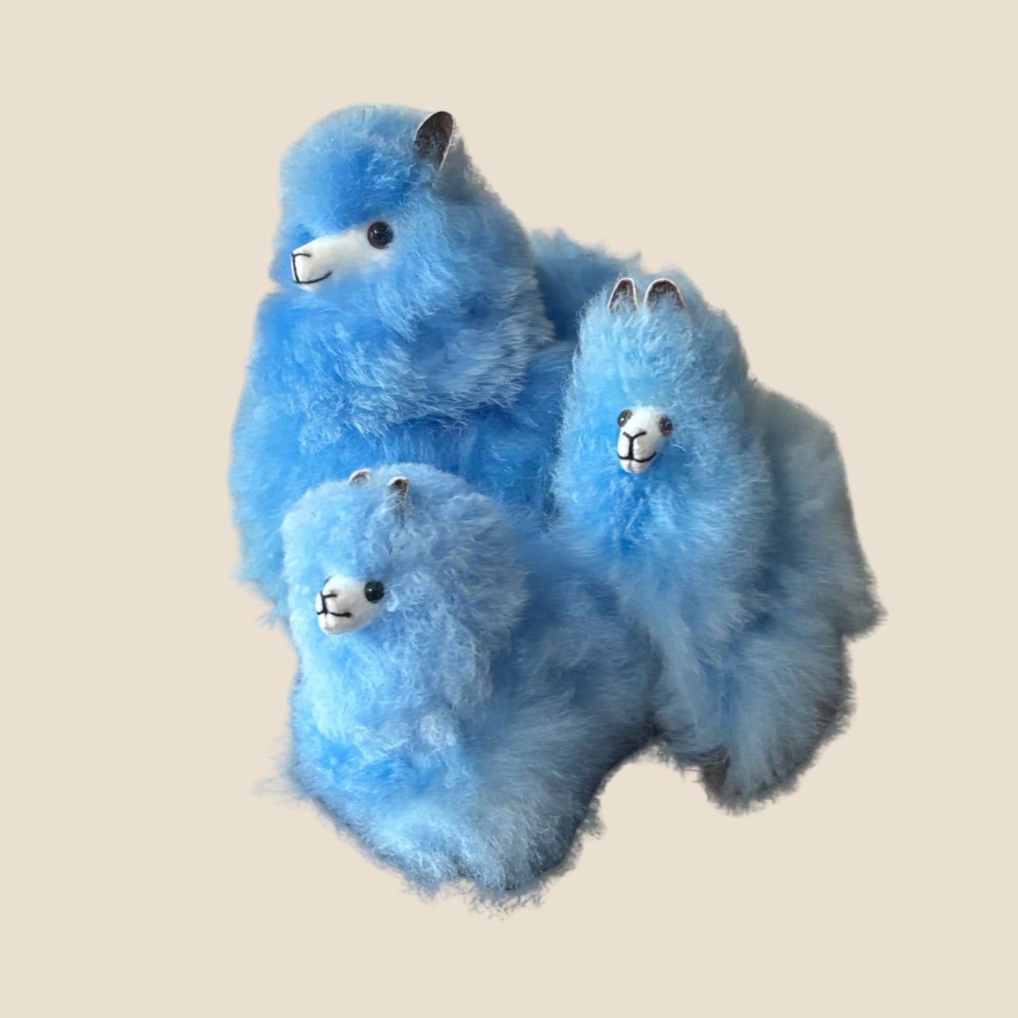 Set of three blue plush alpacas on a beige background