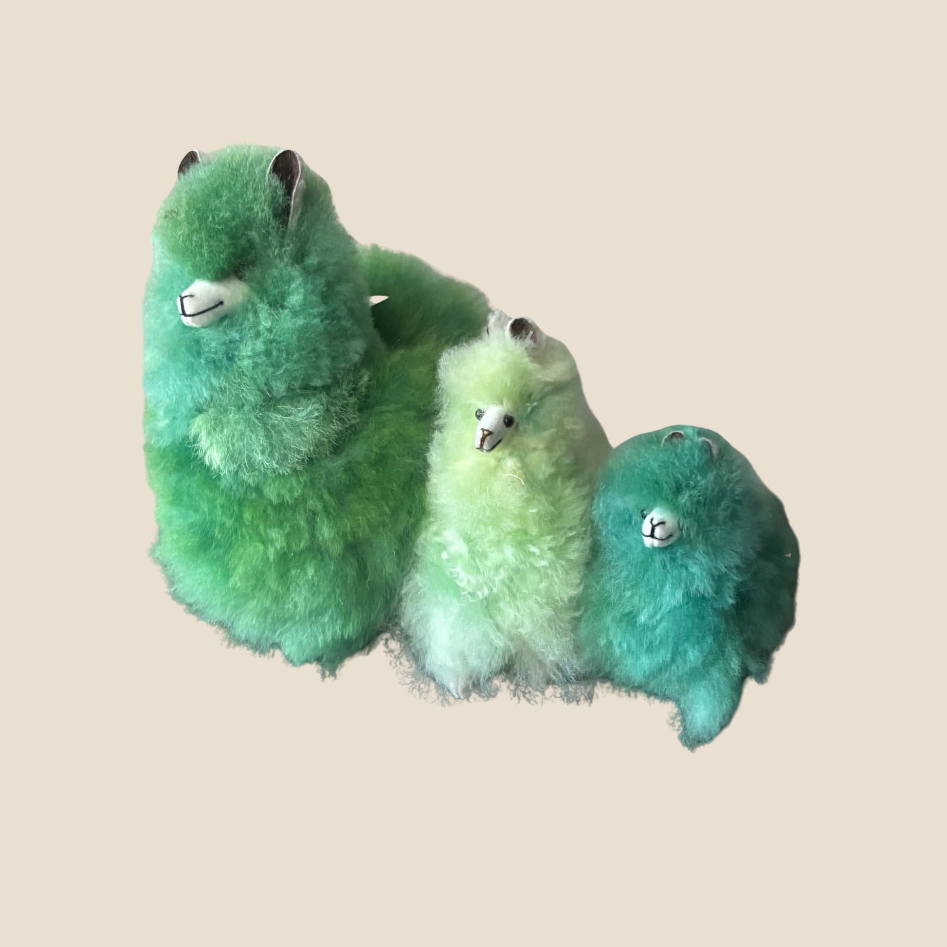 Three green plush toys resembling alpaca  on a beige background