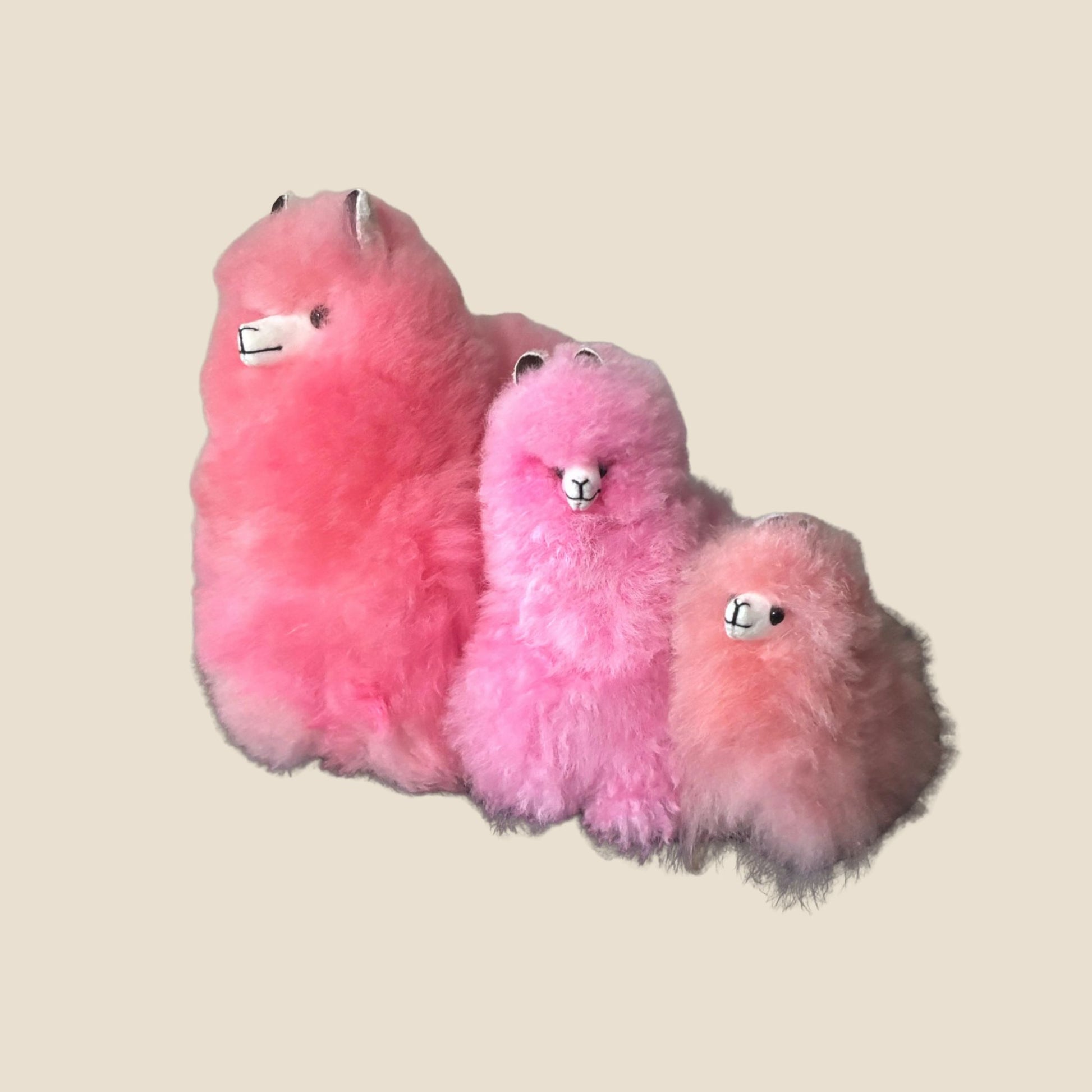 Three pink fluffy toys alpaca on a beige background