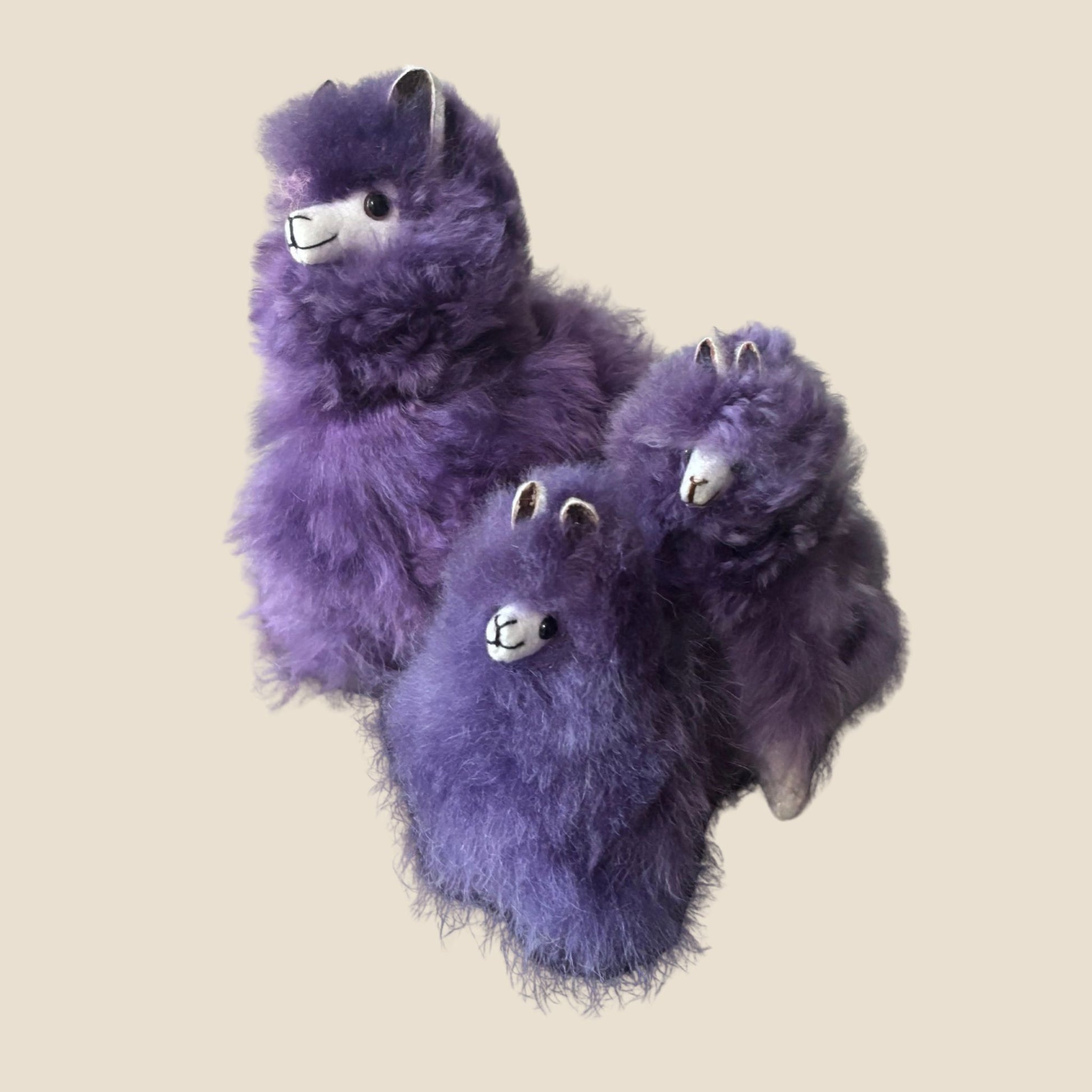 Three purple plush alpaca on a beige background