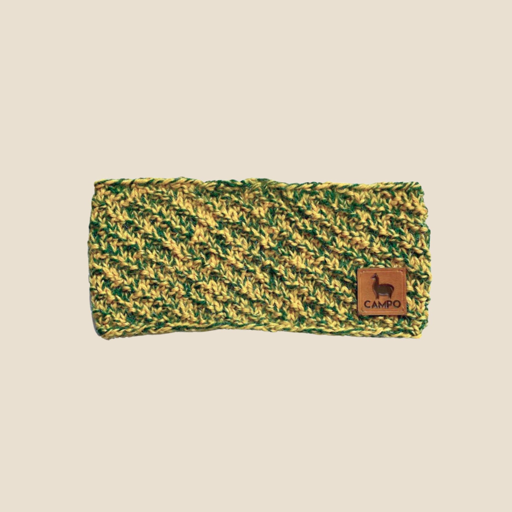 Green and yellow alpaca headband with a brown leather patch on a beige background