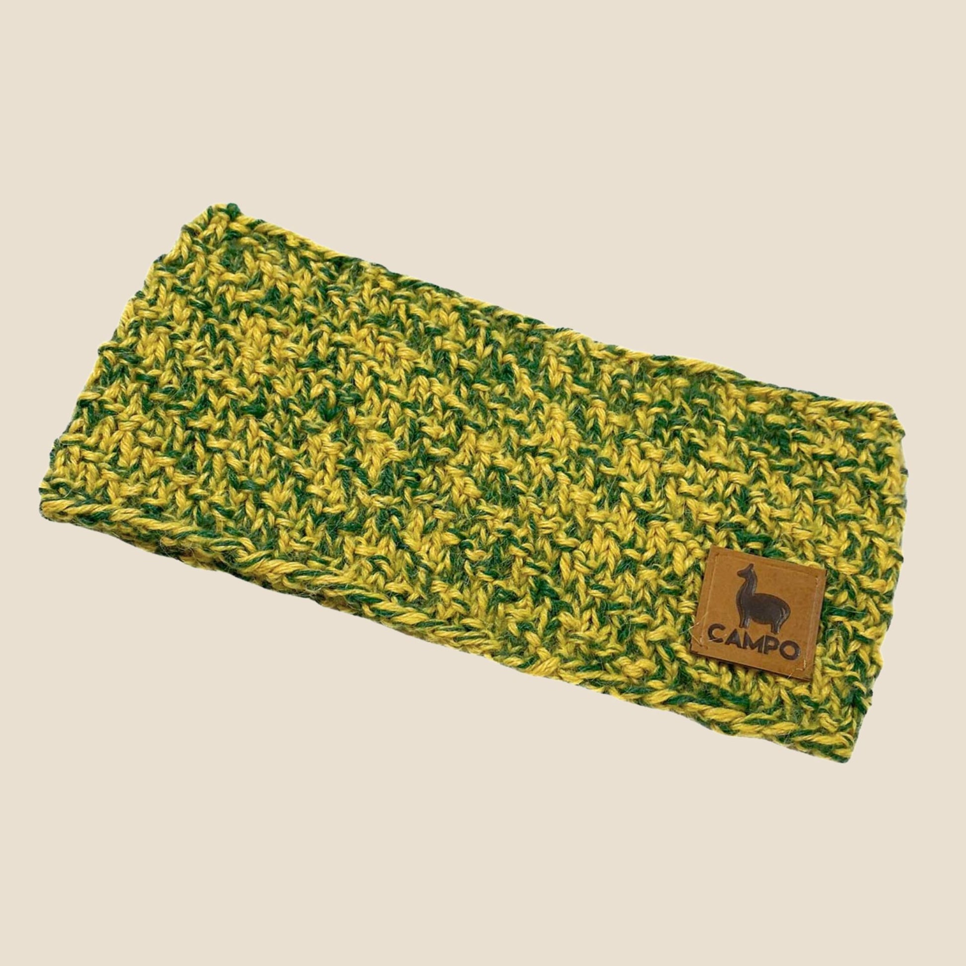 Green and yellow knitted headband with a brown leather patch on a beige background