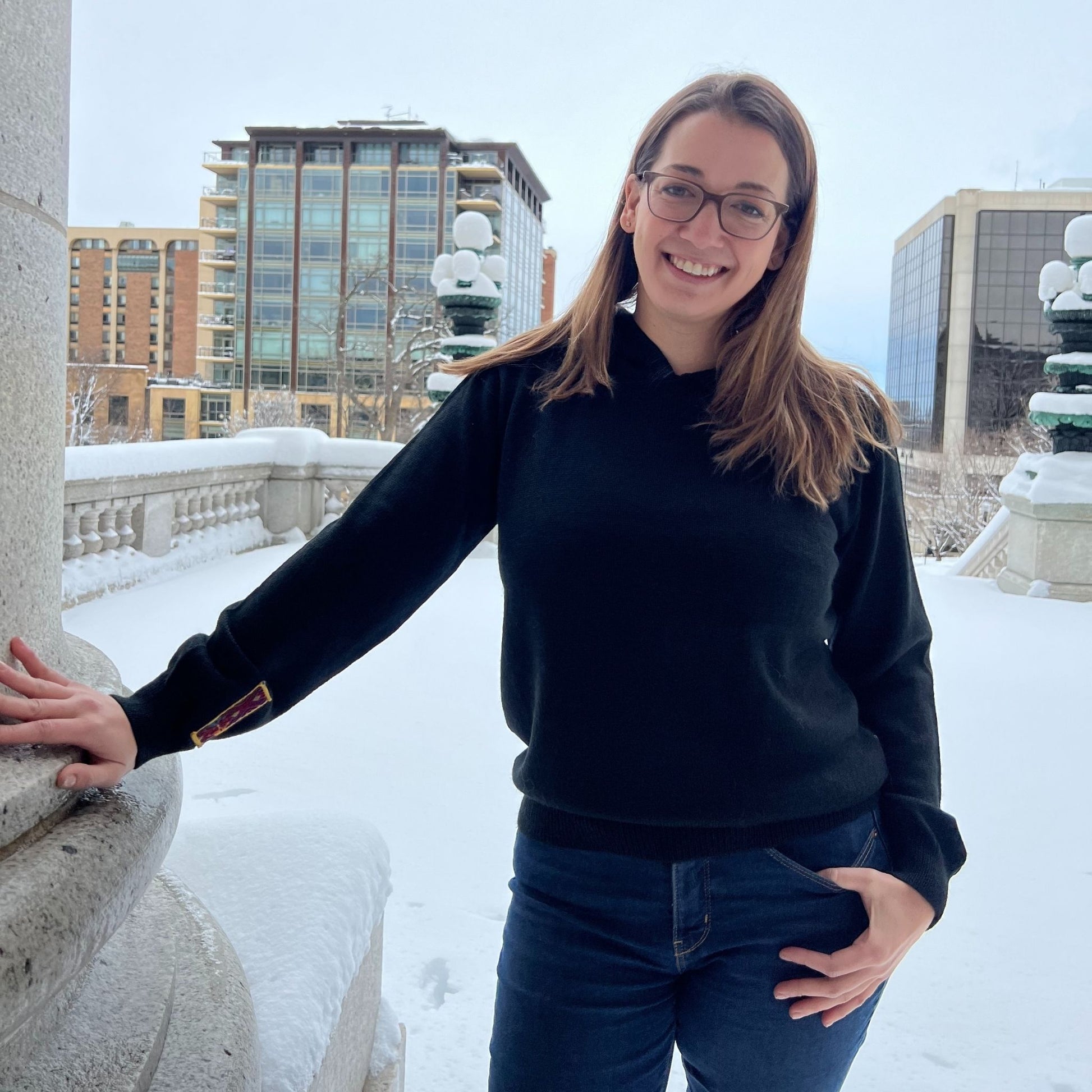 Woman in a black sweater and glasses standing outdoors in a snowy urban setting