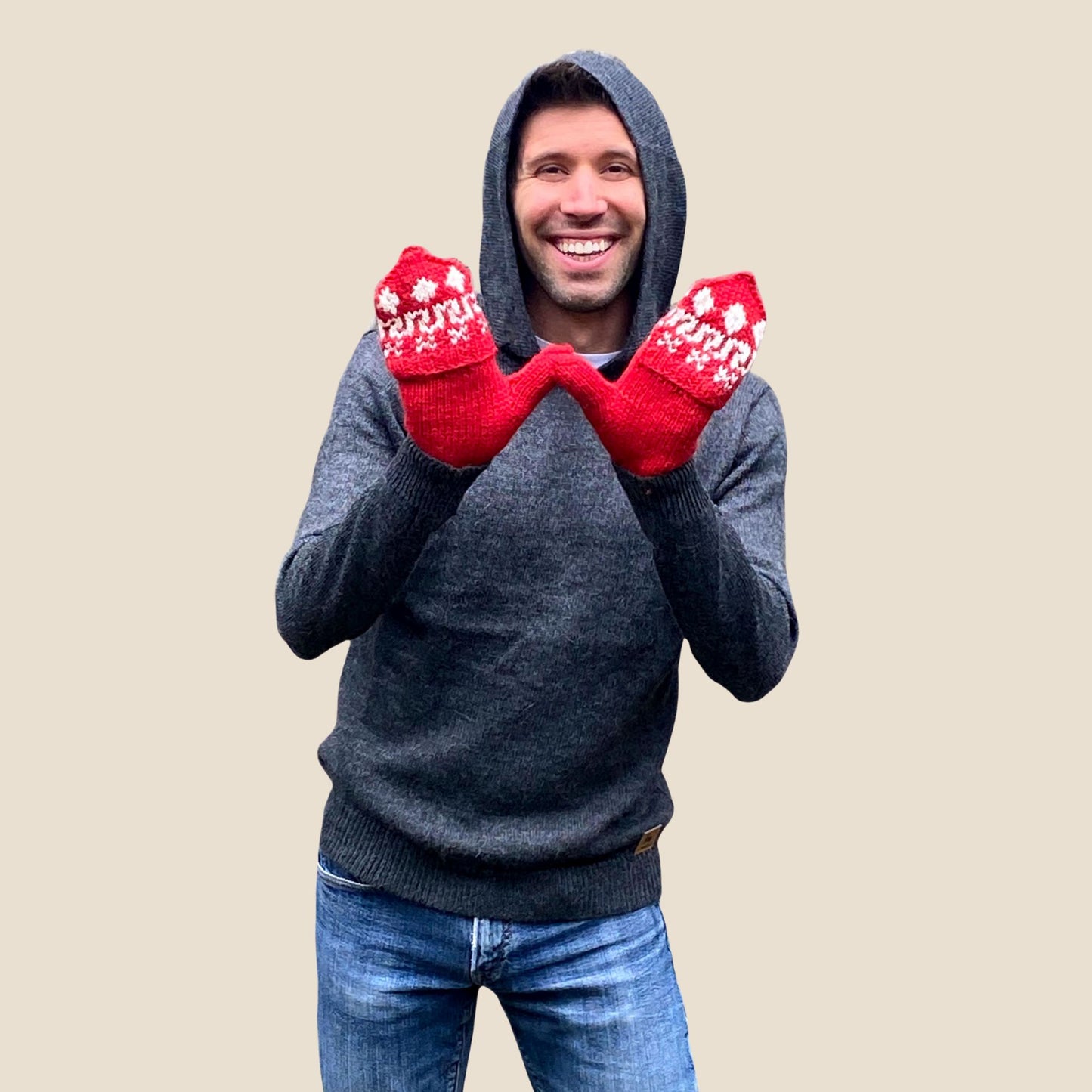 Man wearing a gray hoodie and blue jeans with red mittens on a beige background