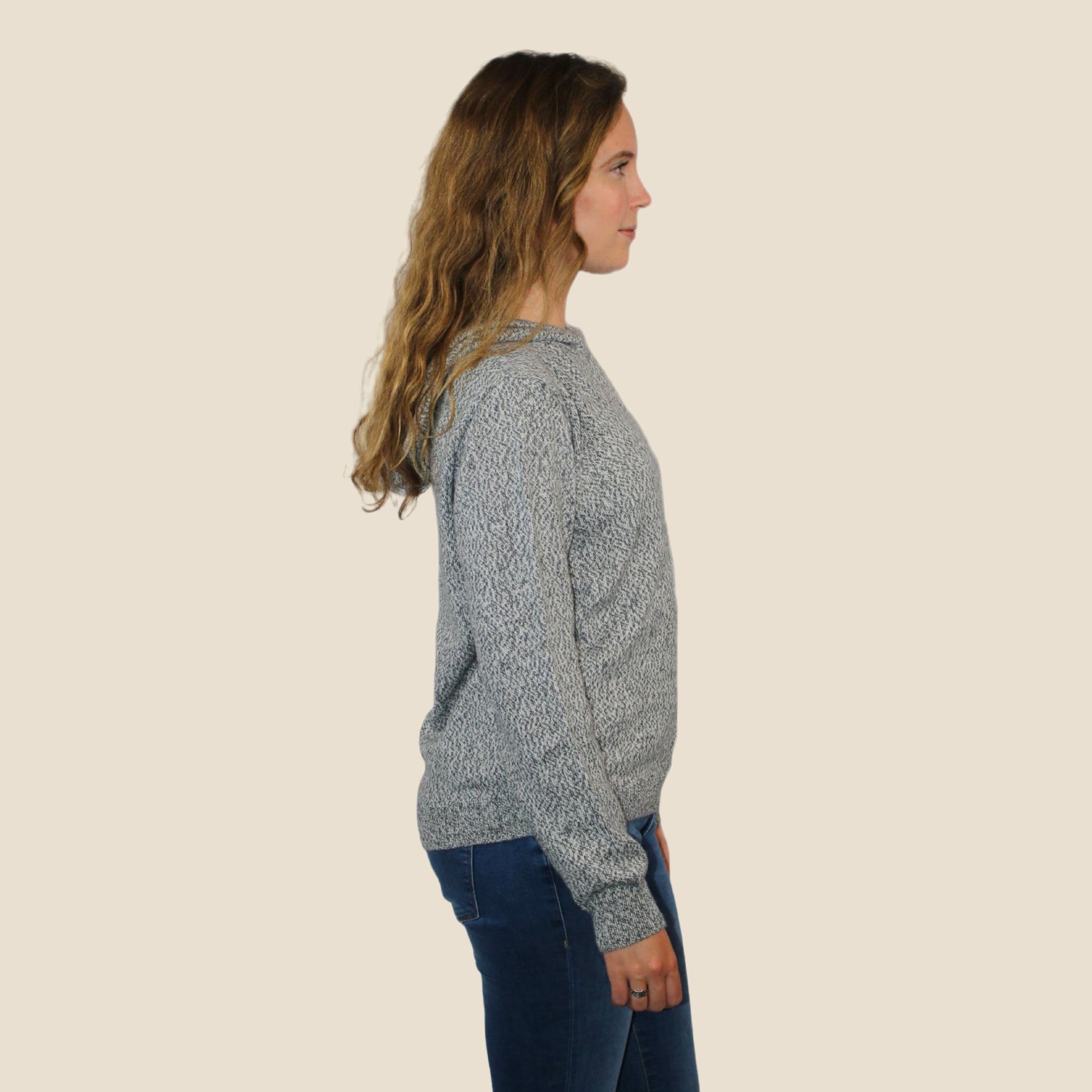 Woman wearing a gray sweater and blue jeans on a beige background
