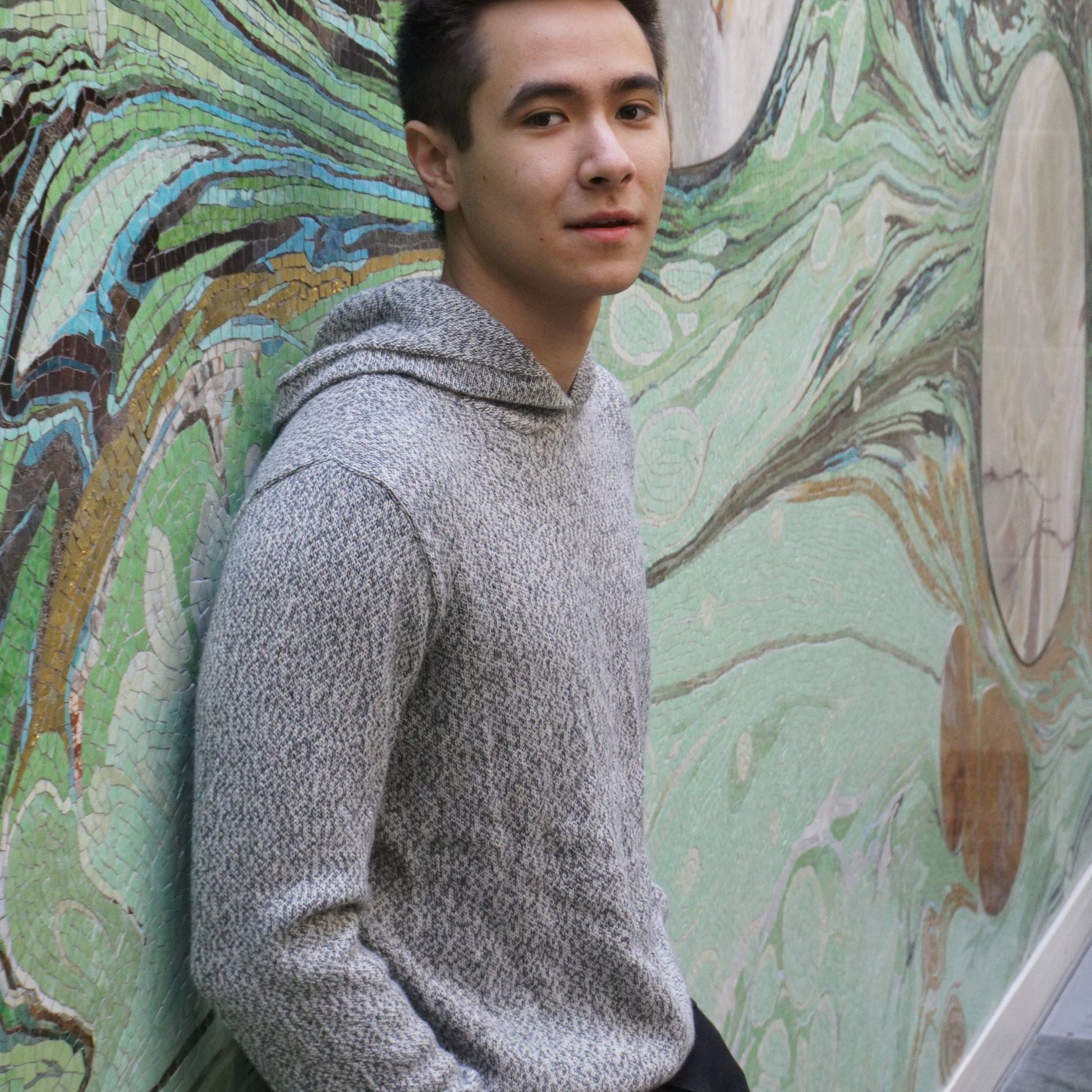 Man wearing a gray hoodie standing against a colorful mural.