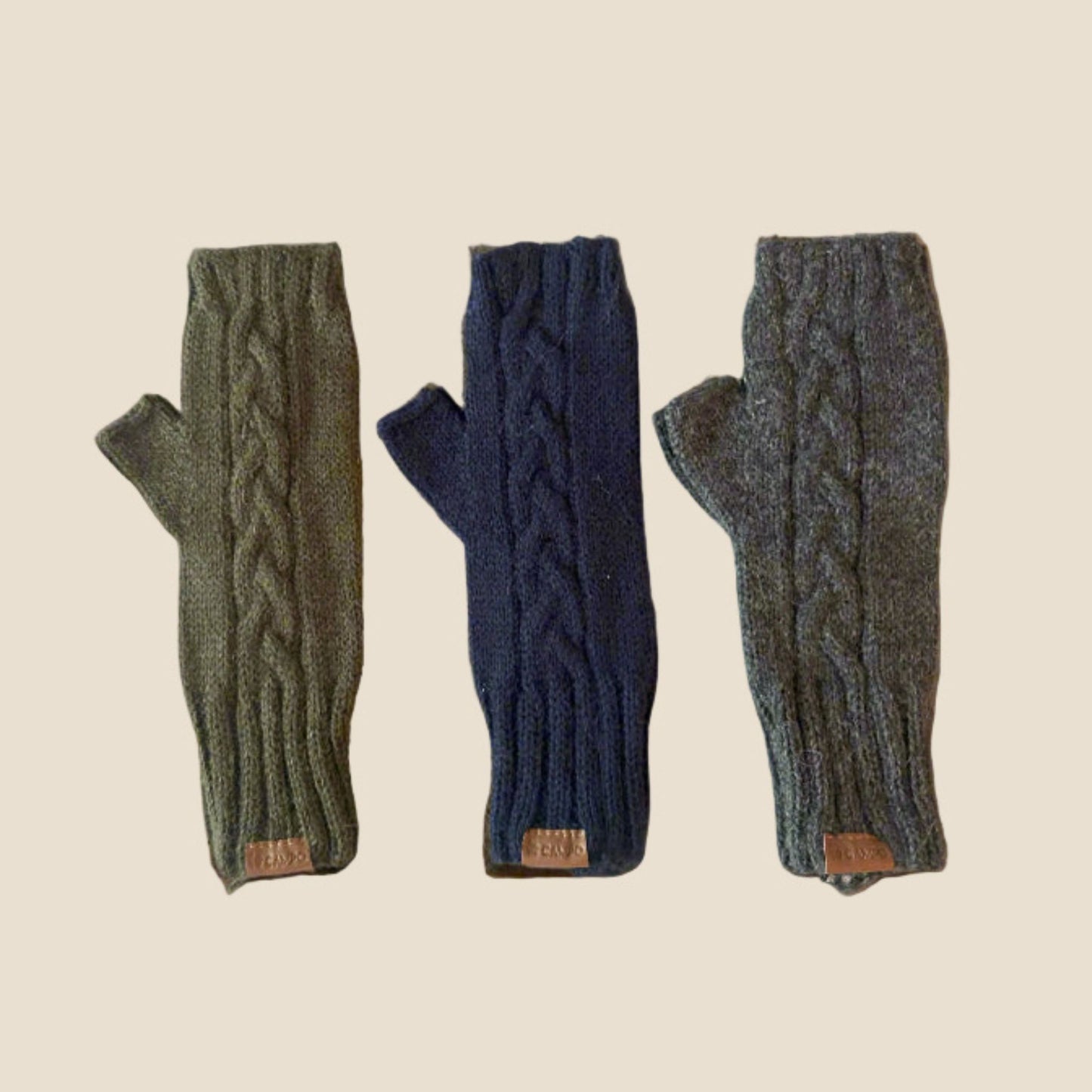 Three pairs of cable knit fingerless gloves in green, blue, and gray on a beige background.