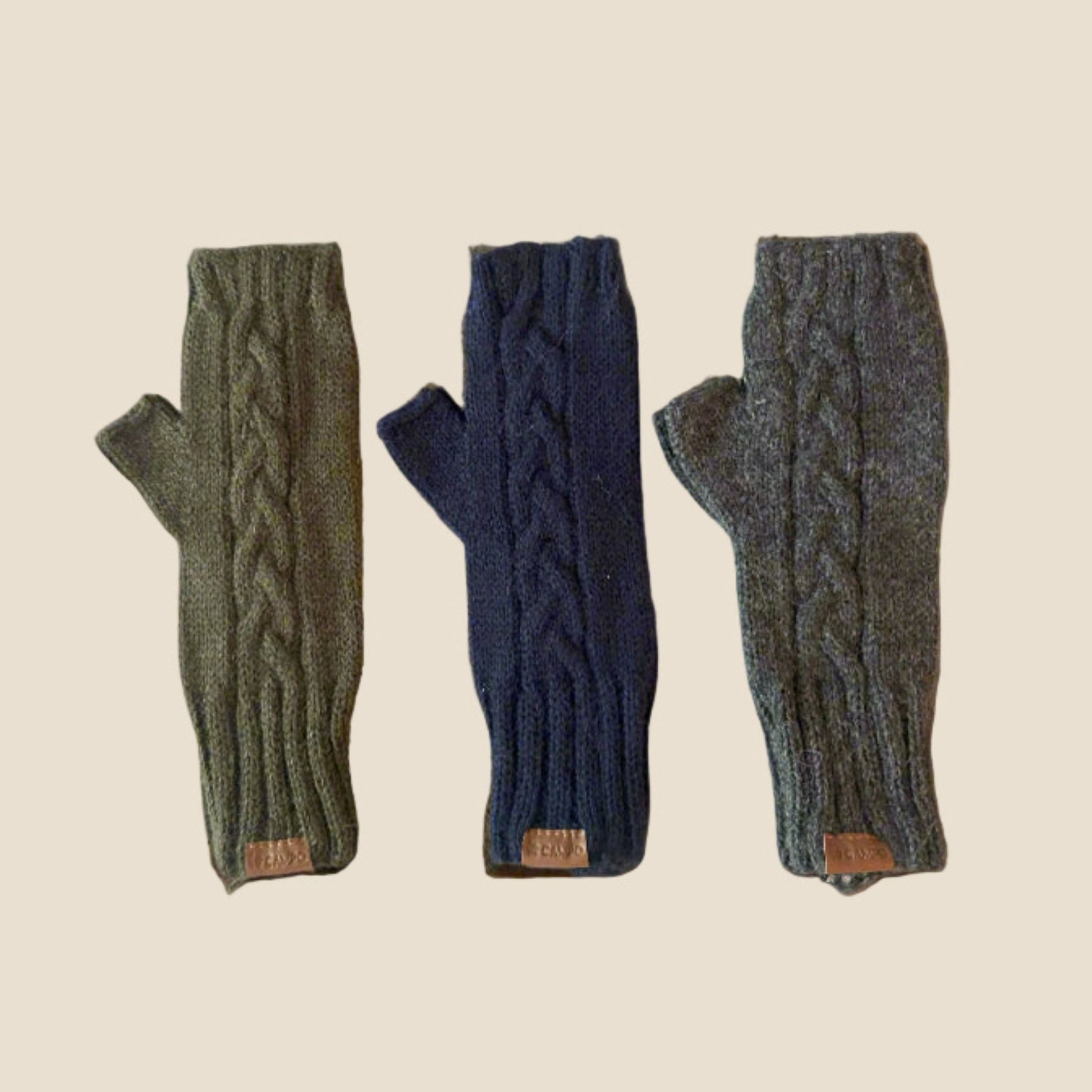 Three pairs of cable knit fingerless gloves in green, blue, and gray on a beige background.