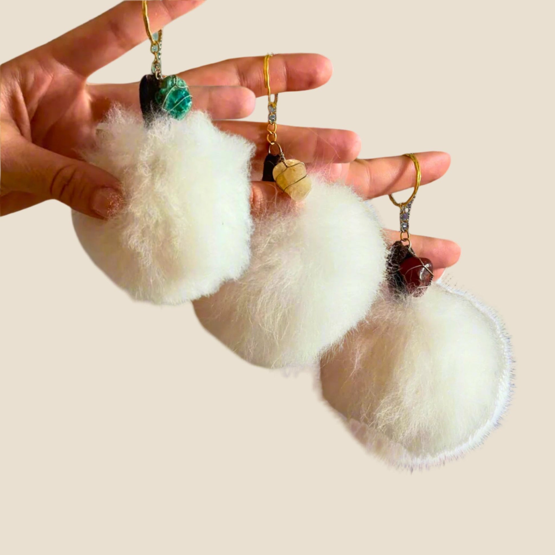 White fluffy keychains held by a hand against a plain background