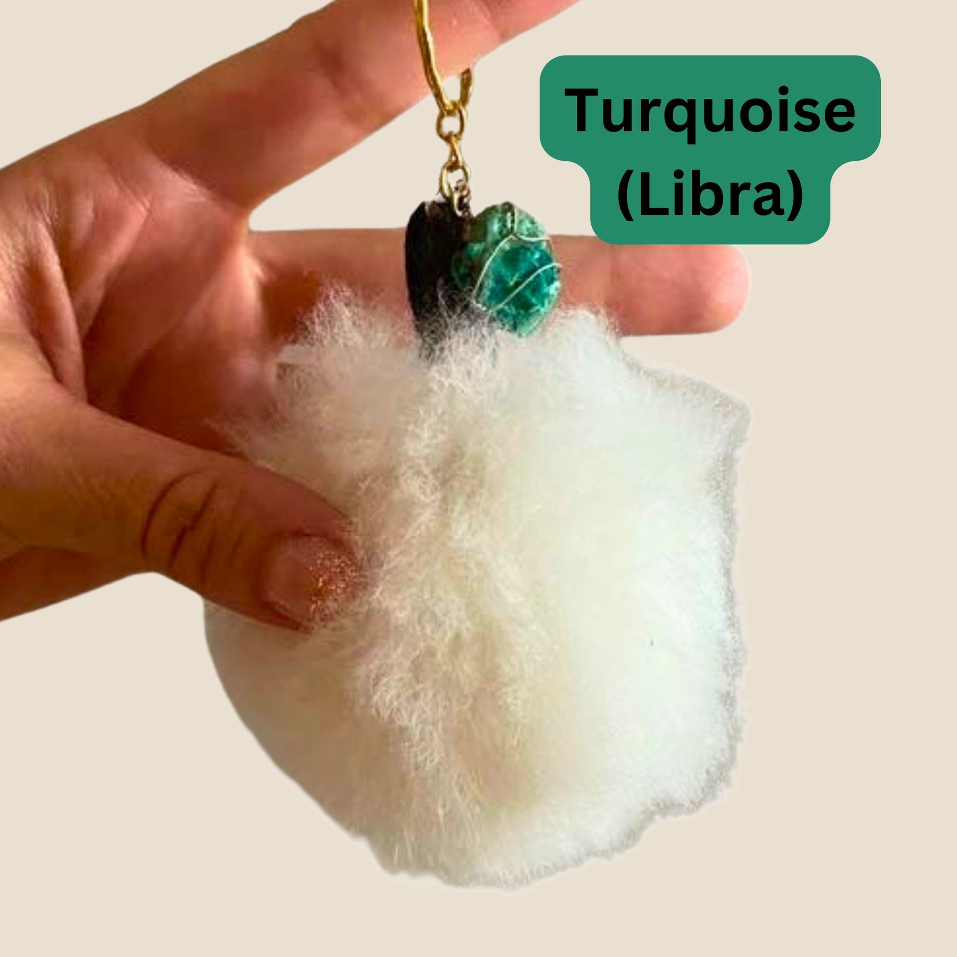 White fluffy keychain with turquoise stone and gold chain held by a hand on a light background