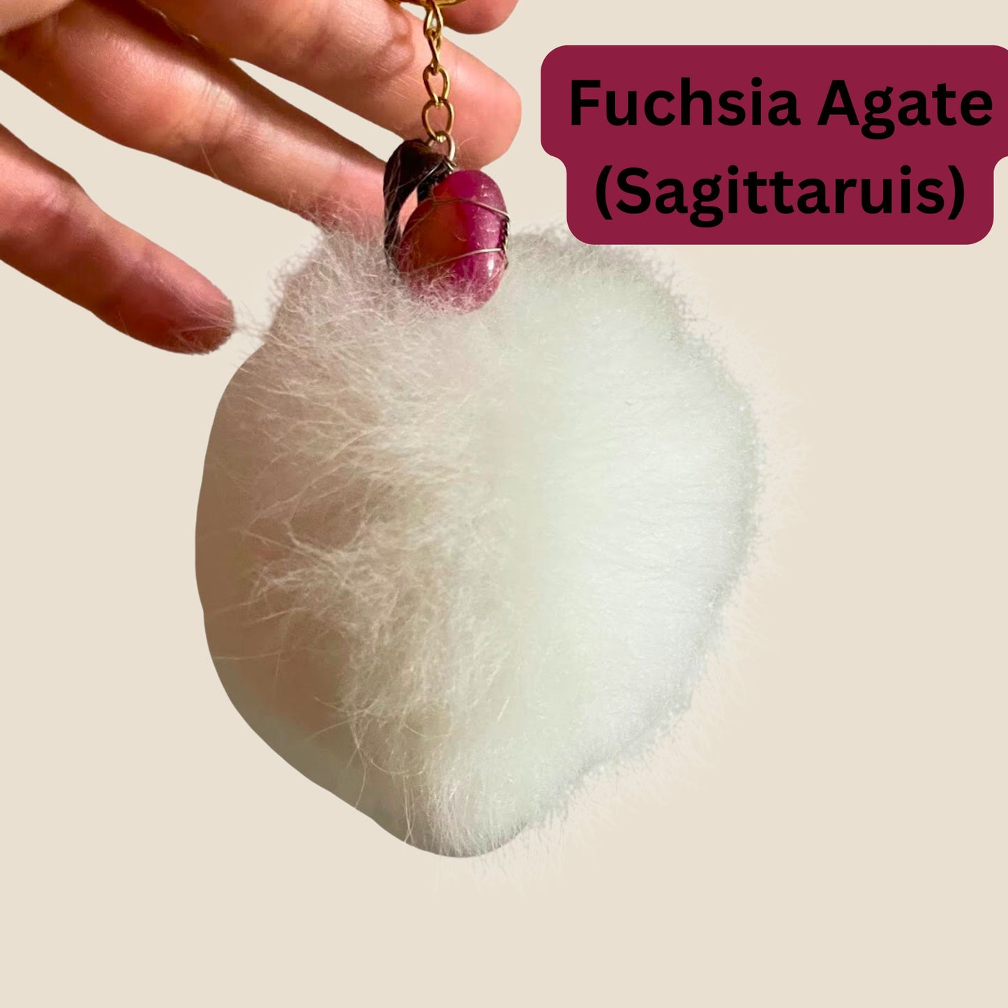 Fuchsia Agate keychain held above a white fluffy on a beige background