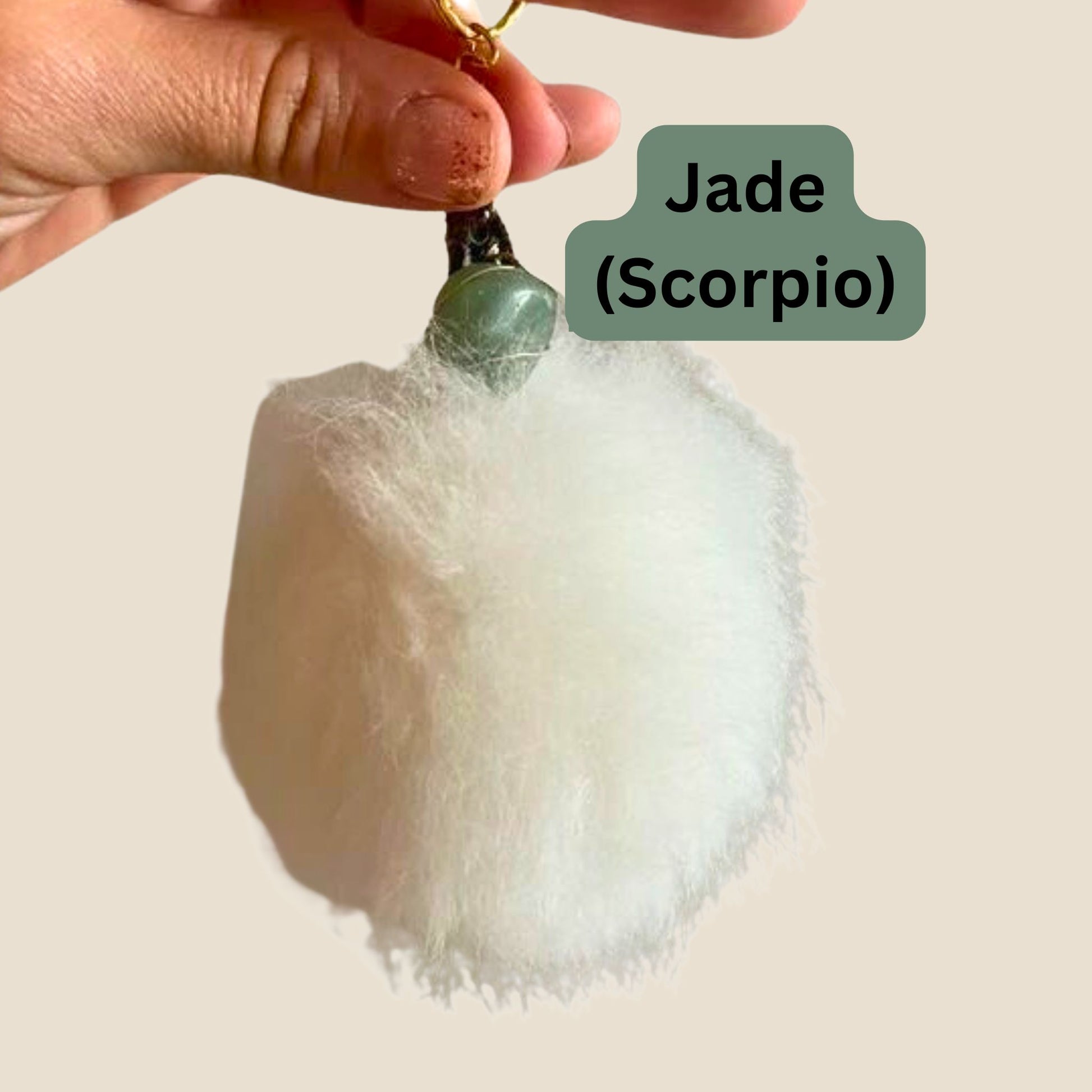 Hand holding a white fluffy keychain with a green gemstone, labeled 'Jade (Scorpio)'.