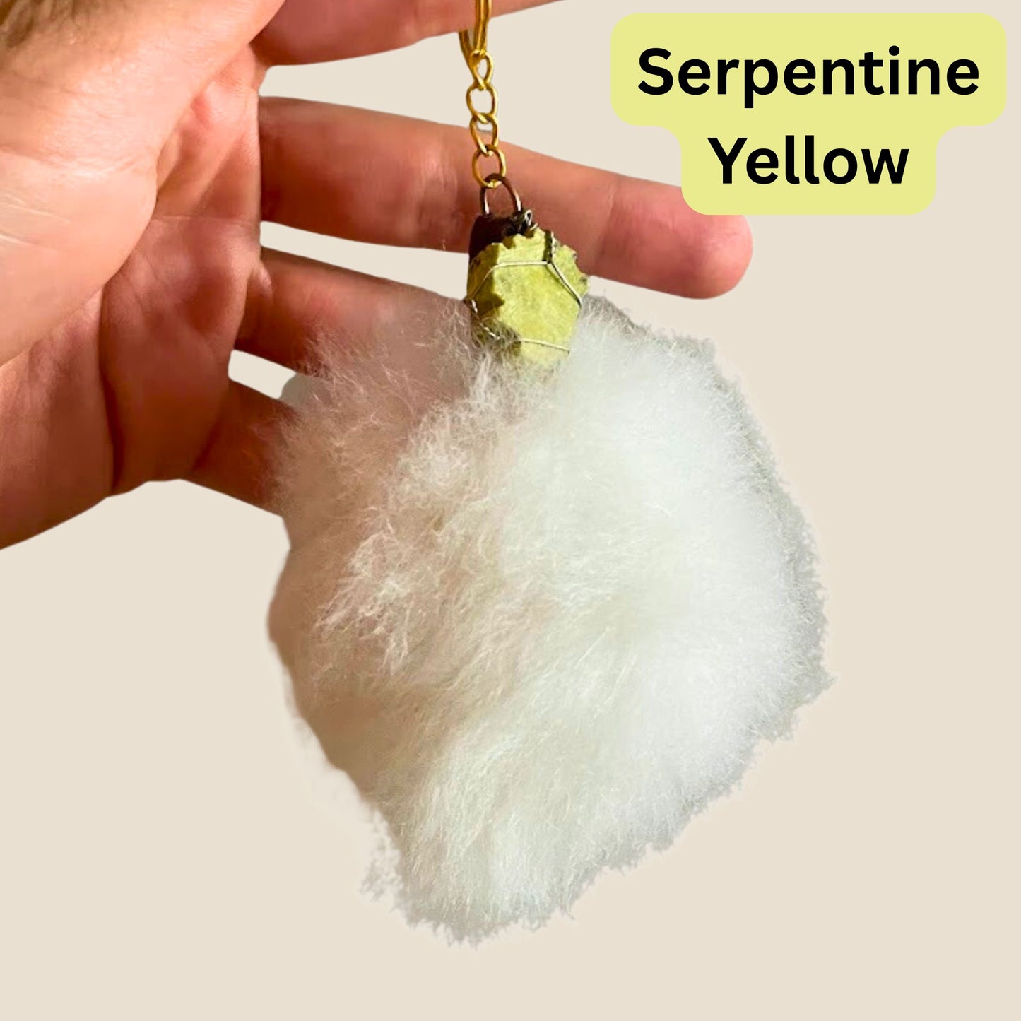 Pom Keychain with a yellow gemstone held by a hand, labeled 'Serpentine Yellow'.