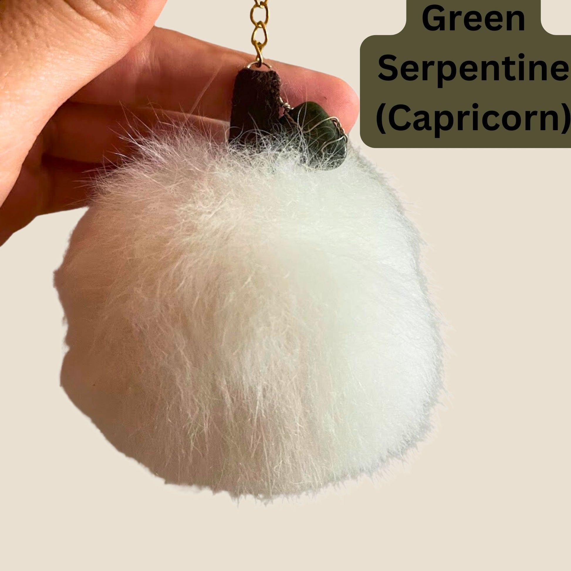 White fluffy keychain with green serpentines and text 'Green Serpentine (Capricorn)' held by a hand.