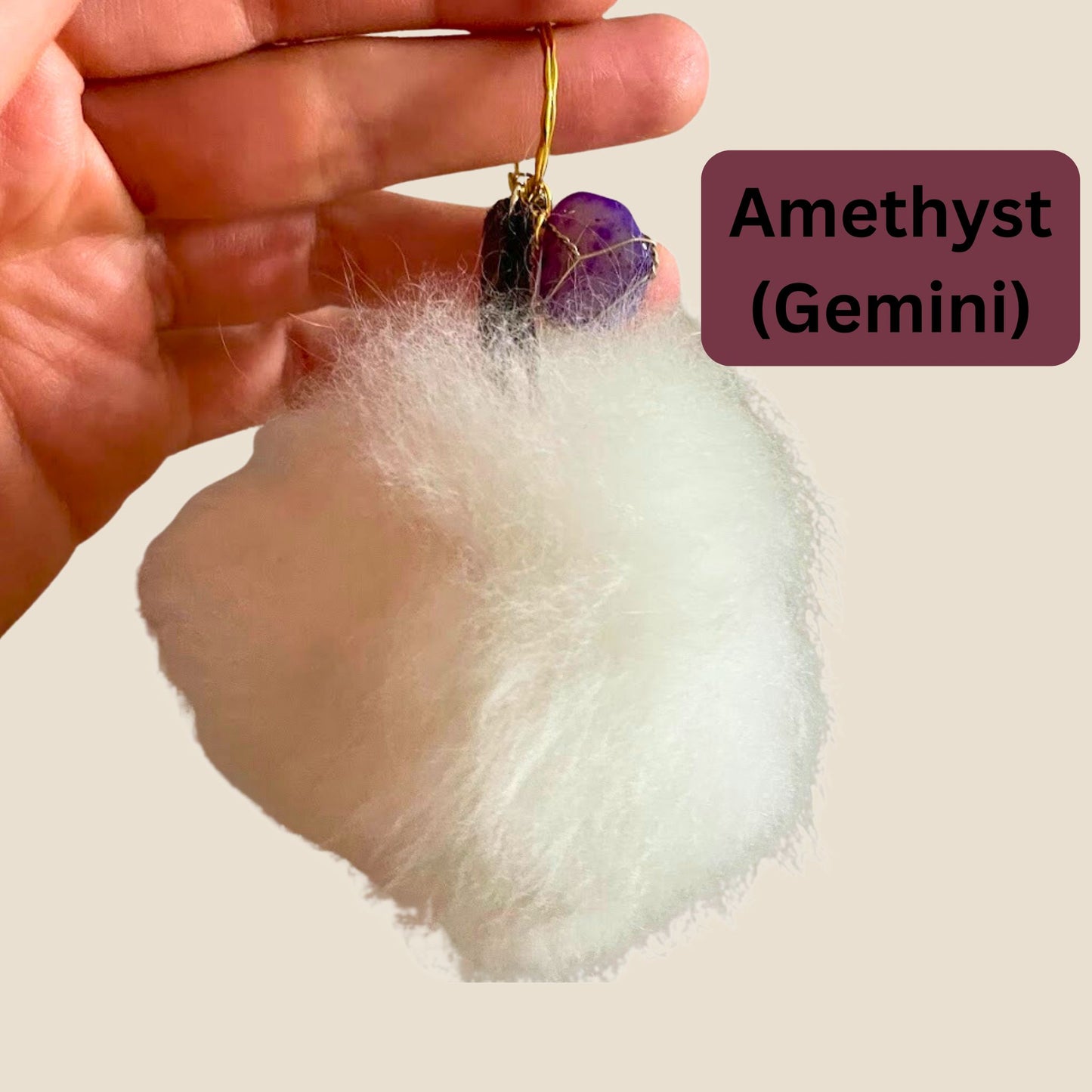 Hand holding a keychain with a white fluff and purple gemstone, labeled 'Amethyst (Gemini)'