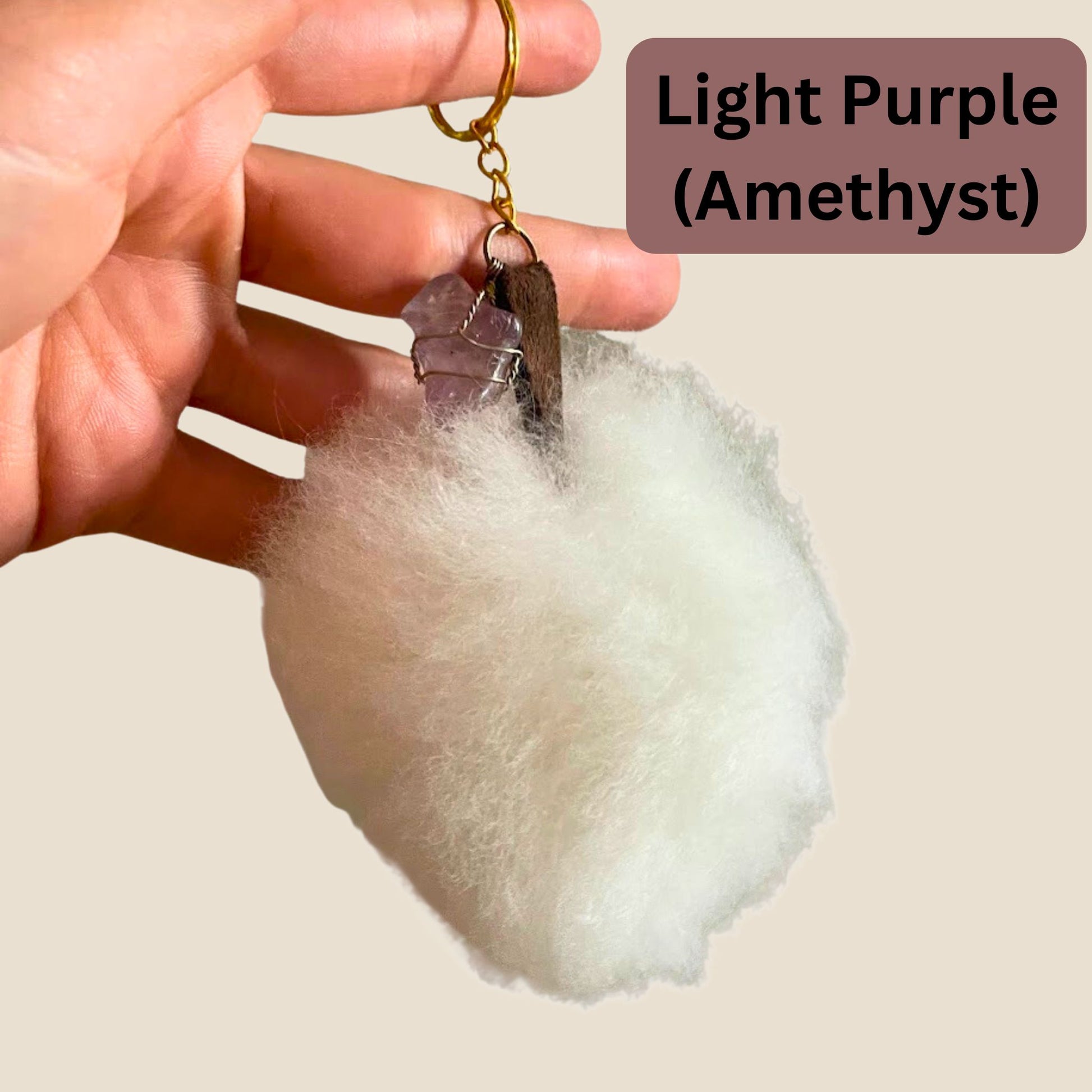 Hand holding a light purple crystal keychain with 'Amethyst' text on a beige background