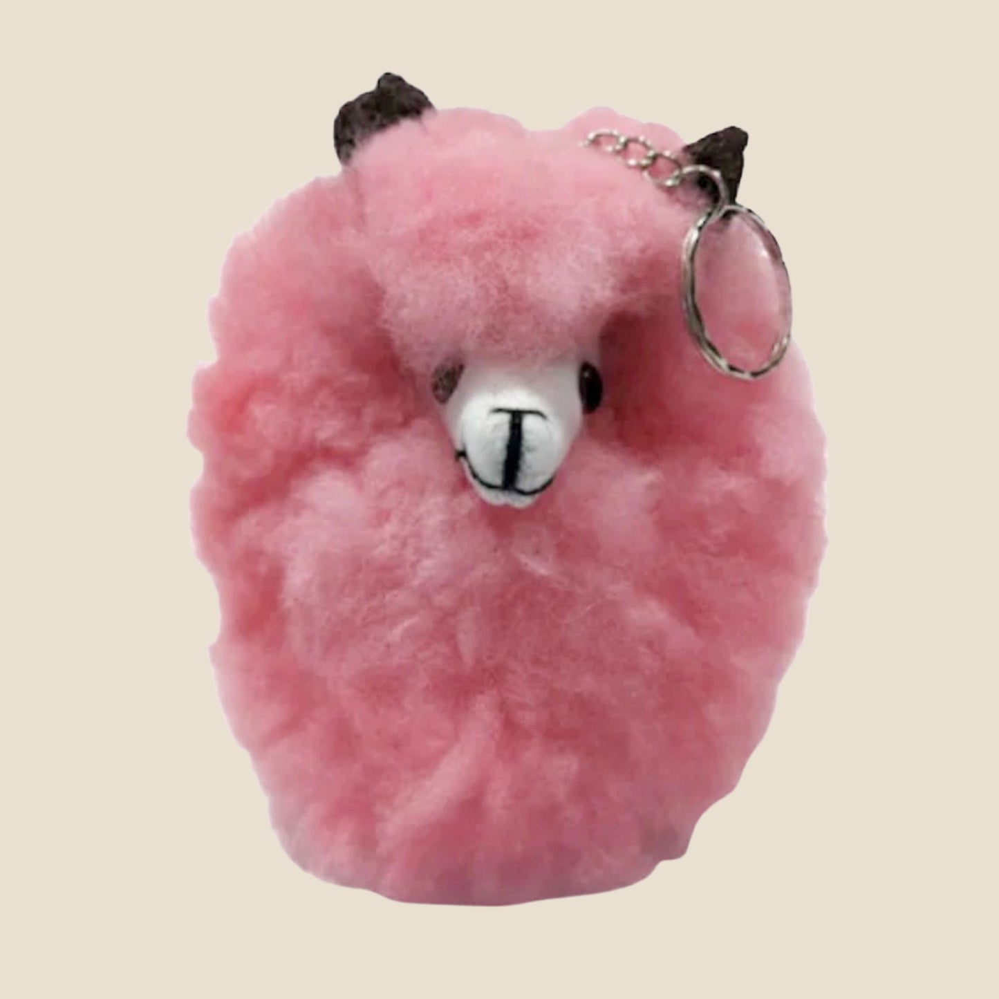 Pink fluffy keychain shaped like a alpaca on a beige background