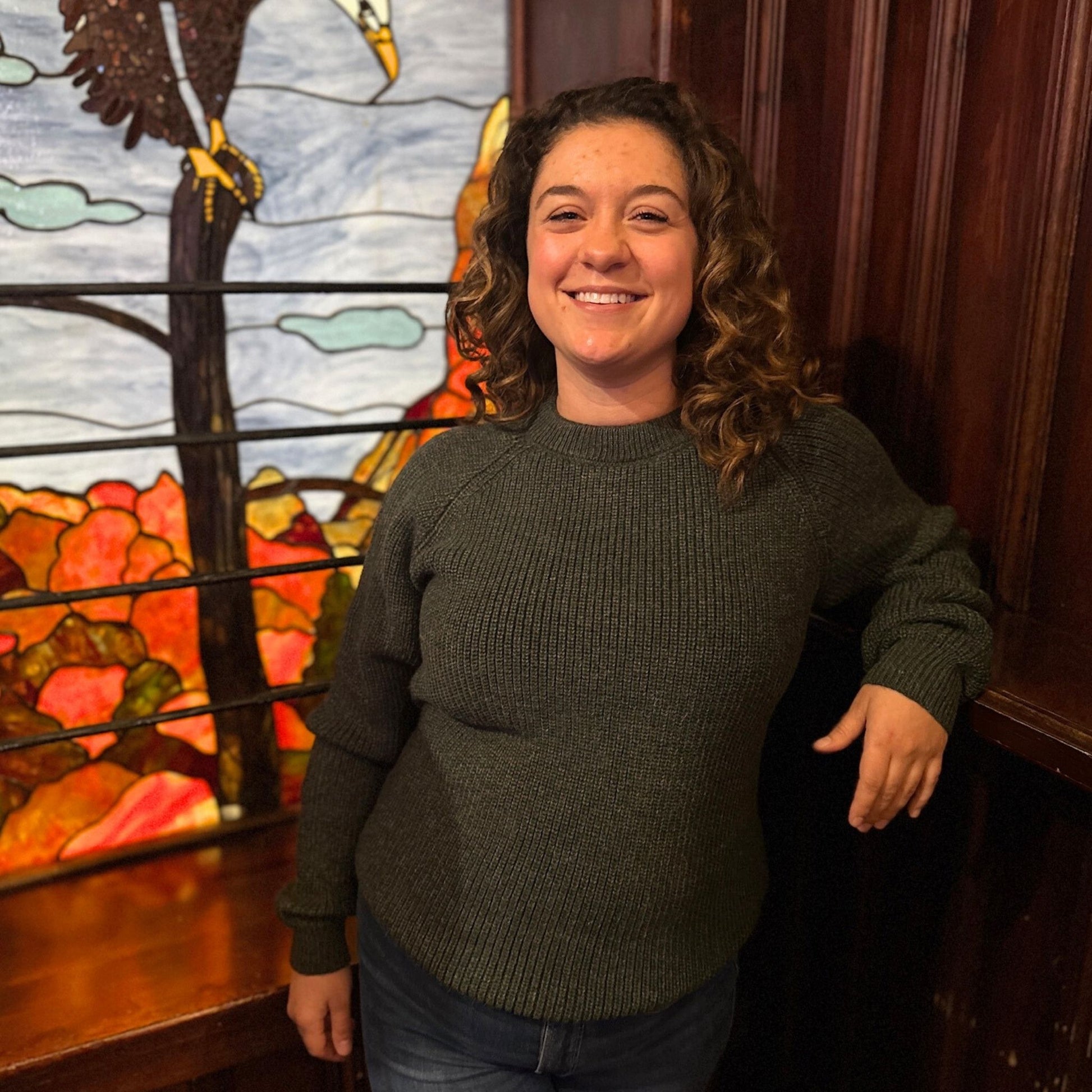 Woman wearing dark green raglan standing in front of a stained glass window