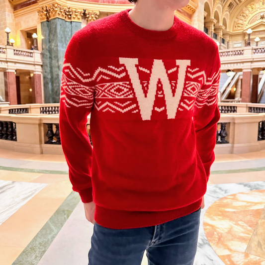 Person wearing a red sweater with a large 'W' in an ornate pattern, standing in a grand hall.
