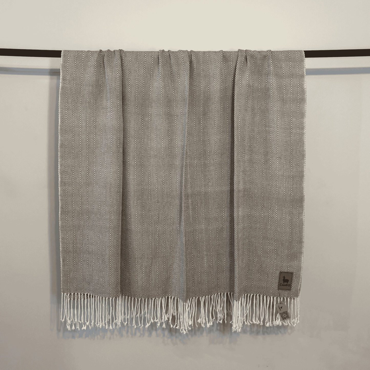 Gray woven blanket with fringes on a black rod against a beige wall