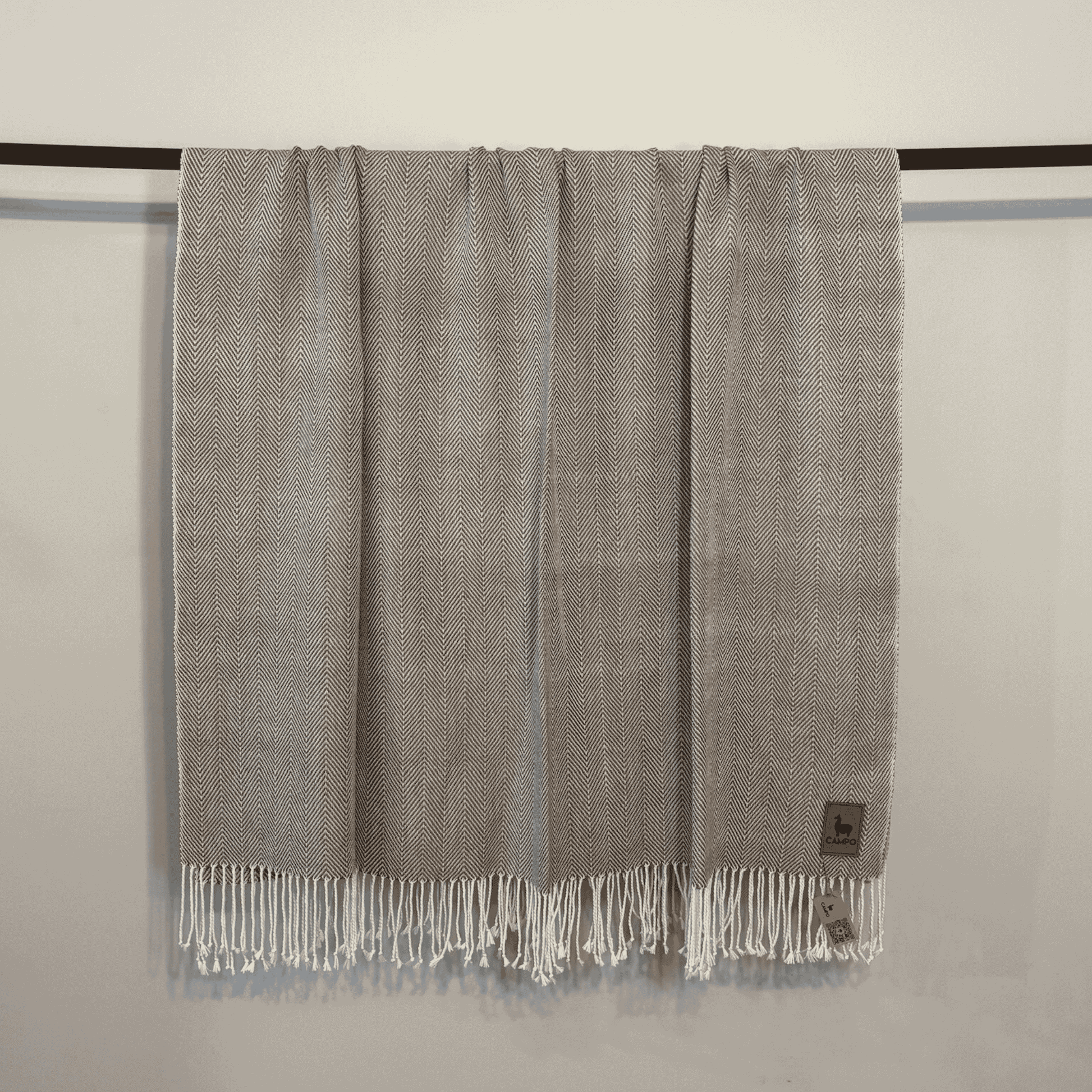 Gray woven blanket with fringes on a black rod against a beige wall