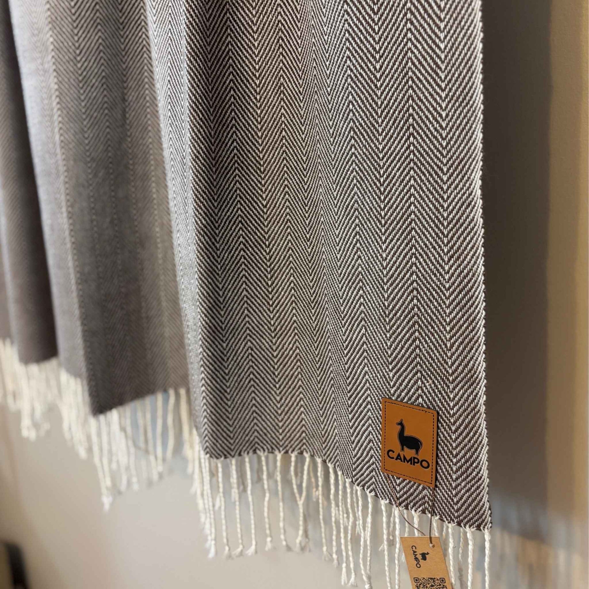 Gray herringbone patterned scarf with a brand label on a neutral background