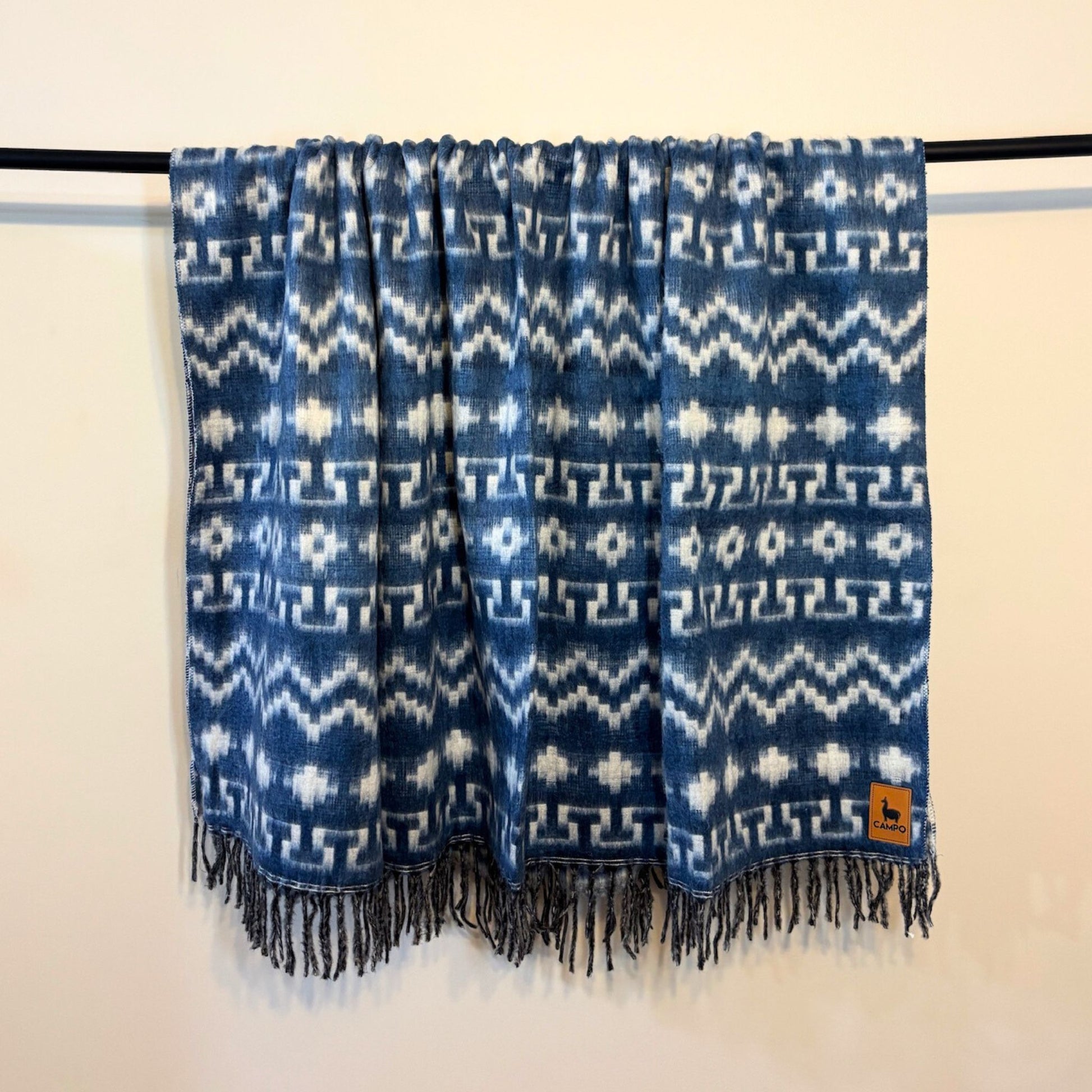 Blue and white patterned scarf with fringes on a black rod against a beige background