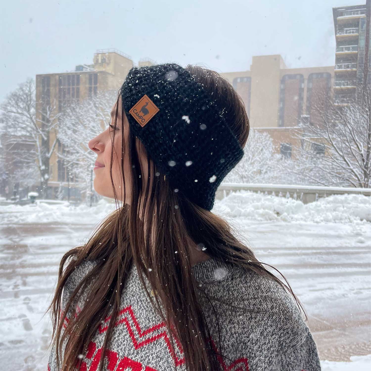 Person wearing a black beanie with a logo in a snowy outdoor setting