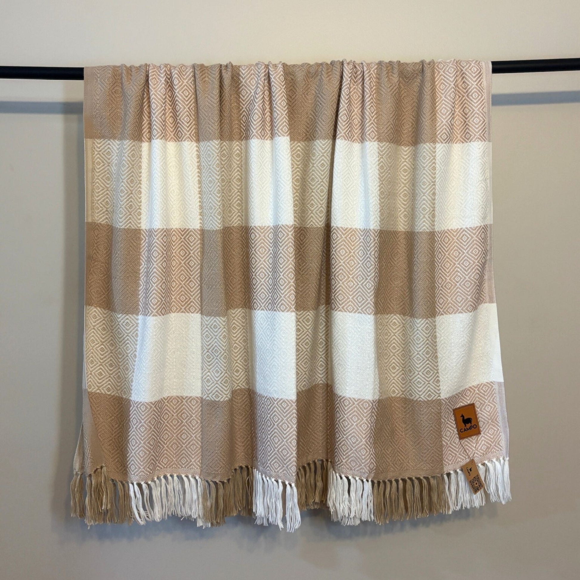 Plaid blanket with fringes on a rack against a plain background
