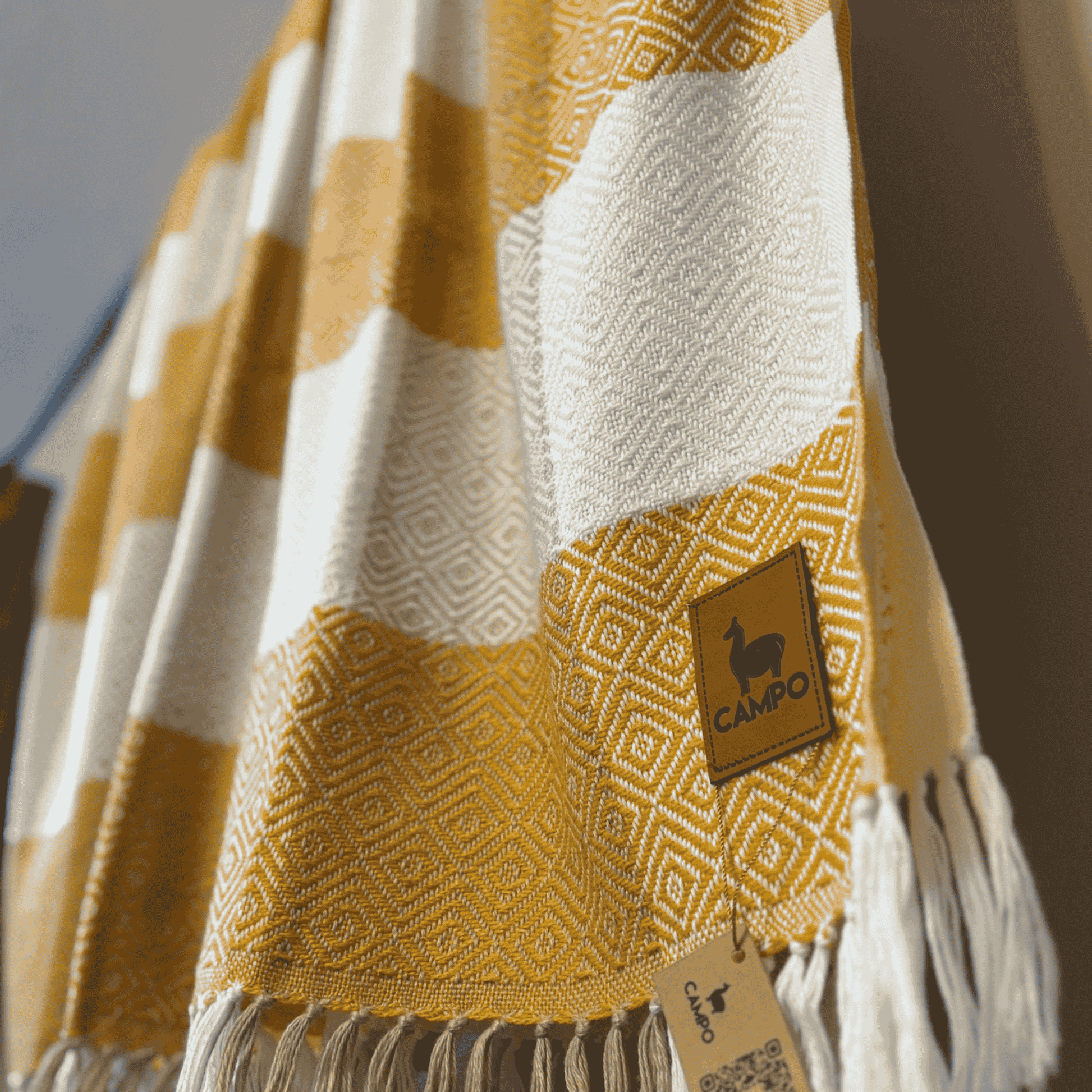 Mustard and white patterned blanket with a 'Campo' brand tag on a blurred background