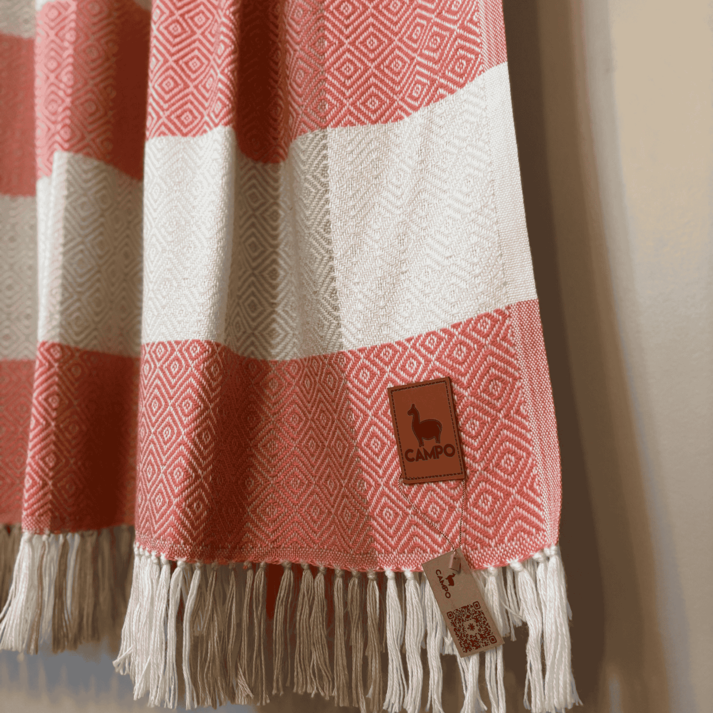Rose and white striped blanket with fringes and a brand tag on a neutral background