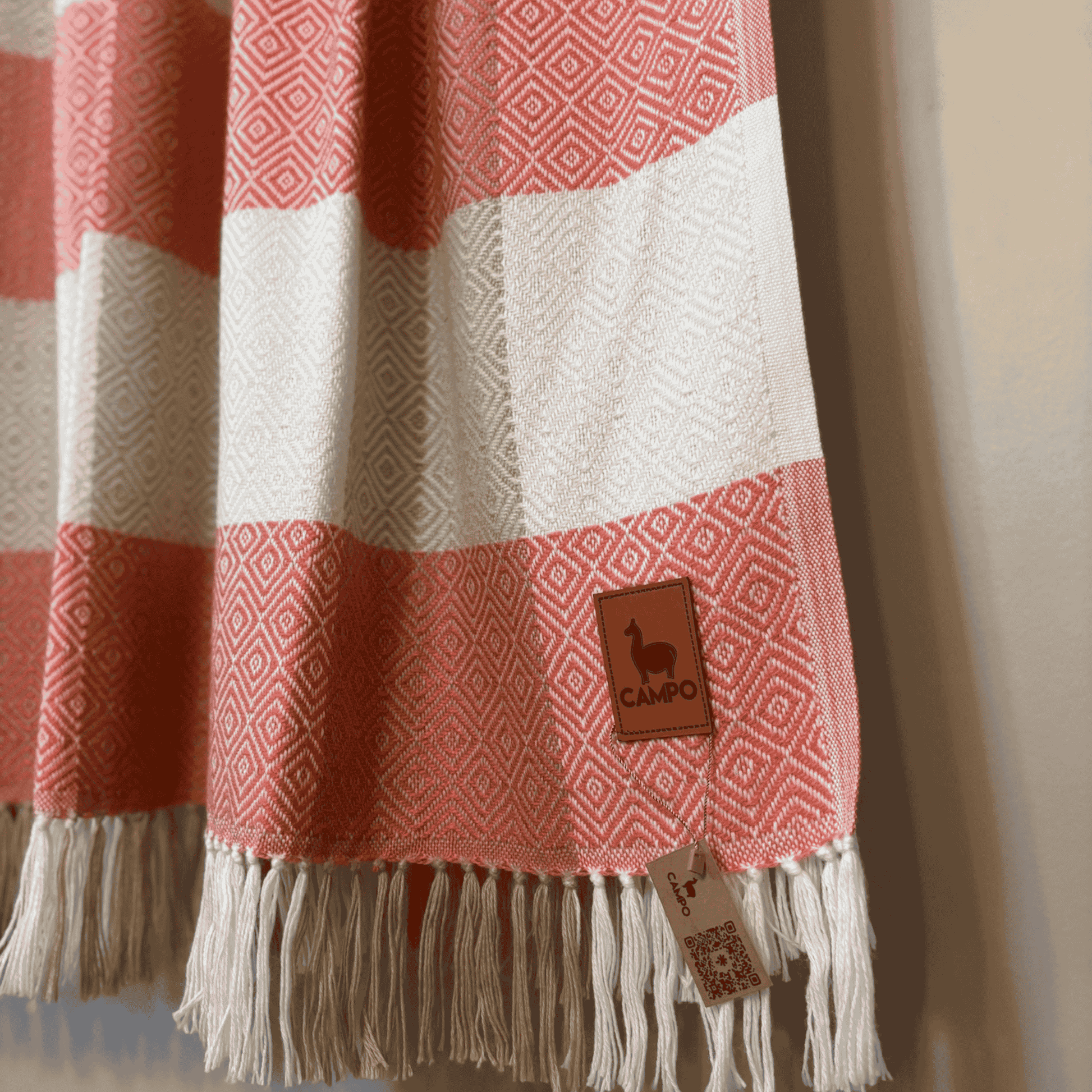 Rose and white striped blanket with fringes and a brand tag on a neutral background