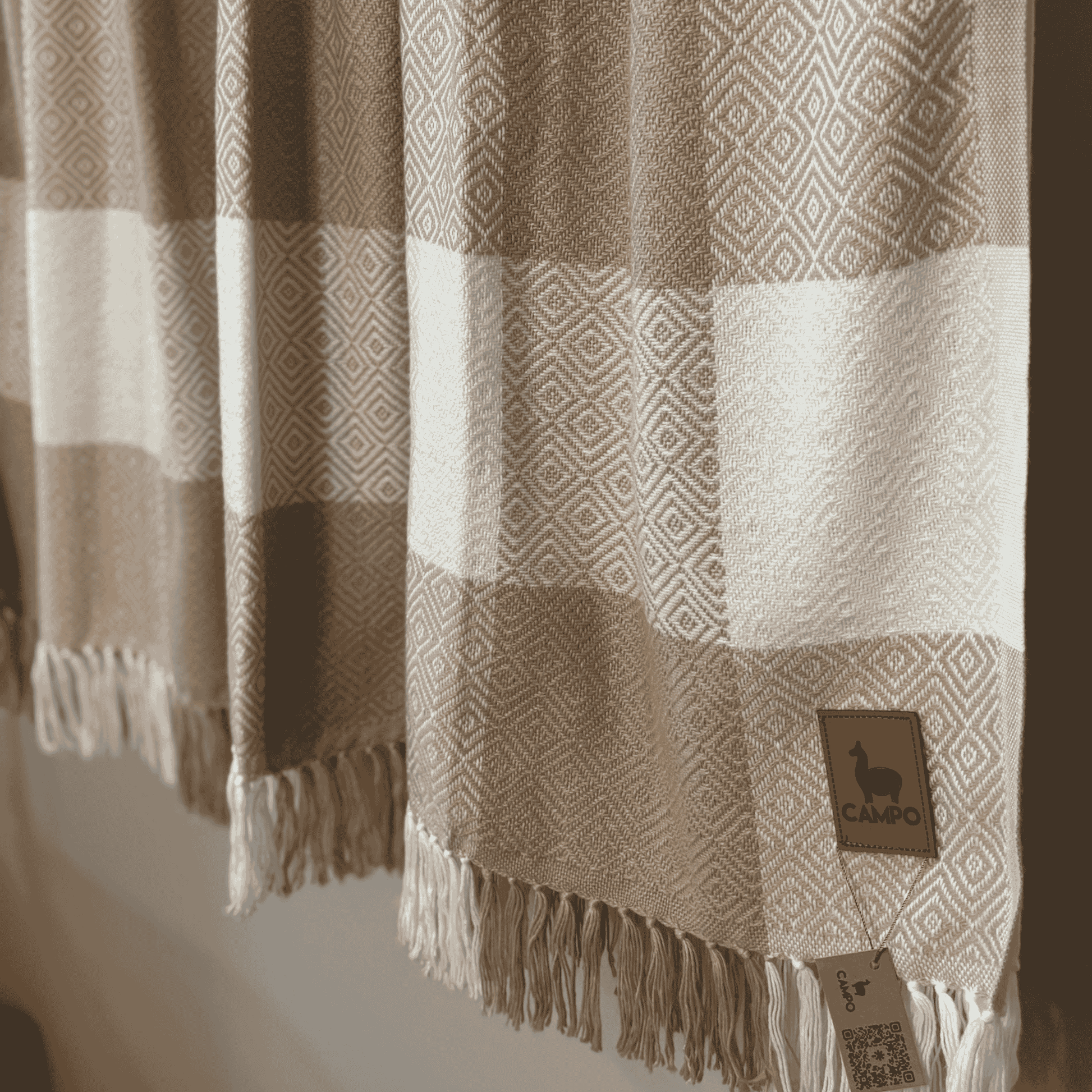 Brown and beige patterned blanket with a brand label on a neutral background
