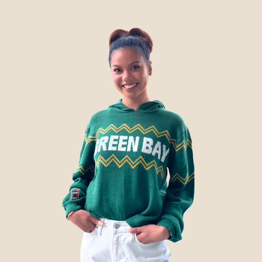 Person wearing a green 'Green Bay' sweater on a beige background