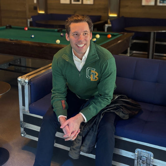 Man in a green jacket with a logo sitting on a blue couch in a pool hall.