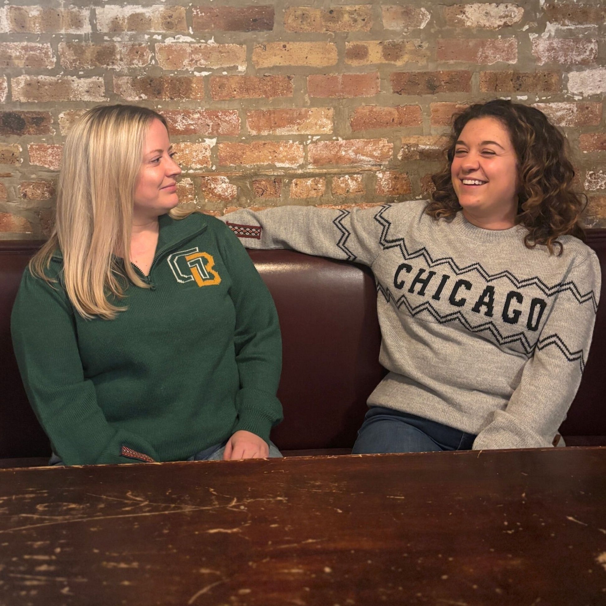 Two women sitting at a table with a brick wall background