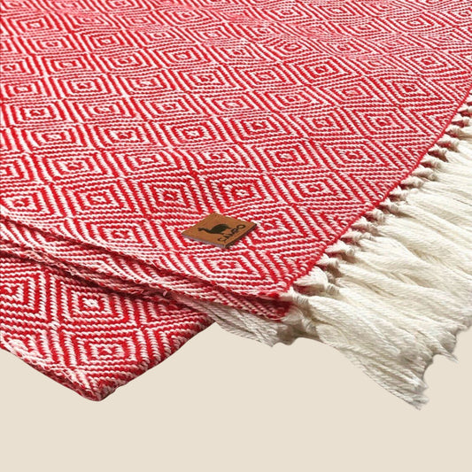 Red and white patterned blanket with a brand logo on a beige background