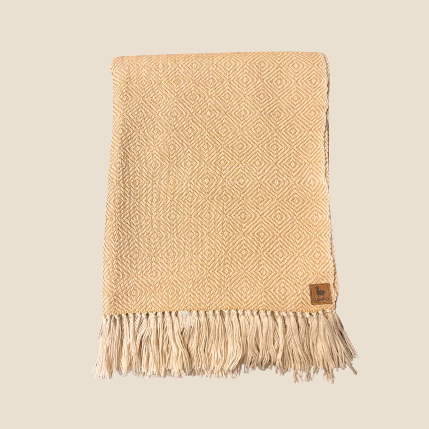 Beige woven blanket with diamond pattern and fringes on a beige background