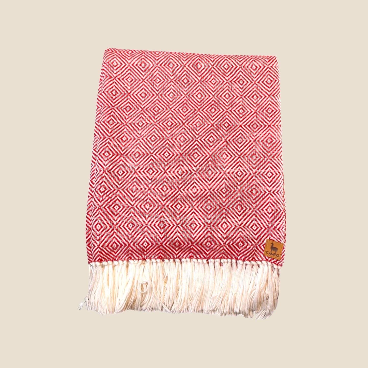 Red and white patterned throw blanket with fringes on a beige background