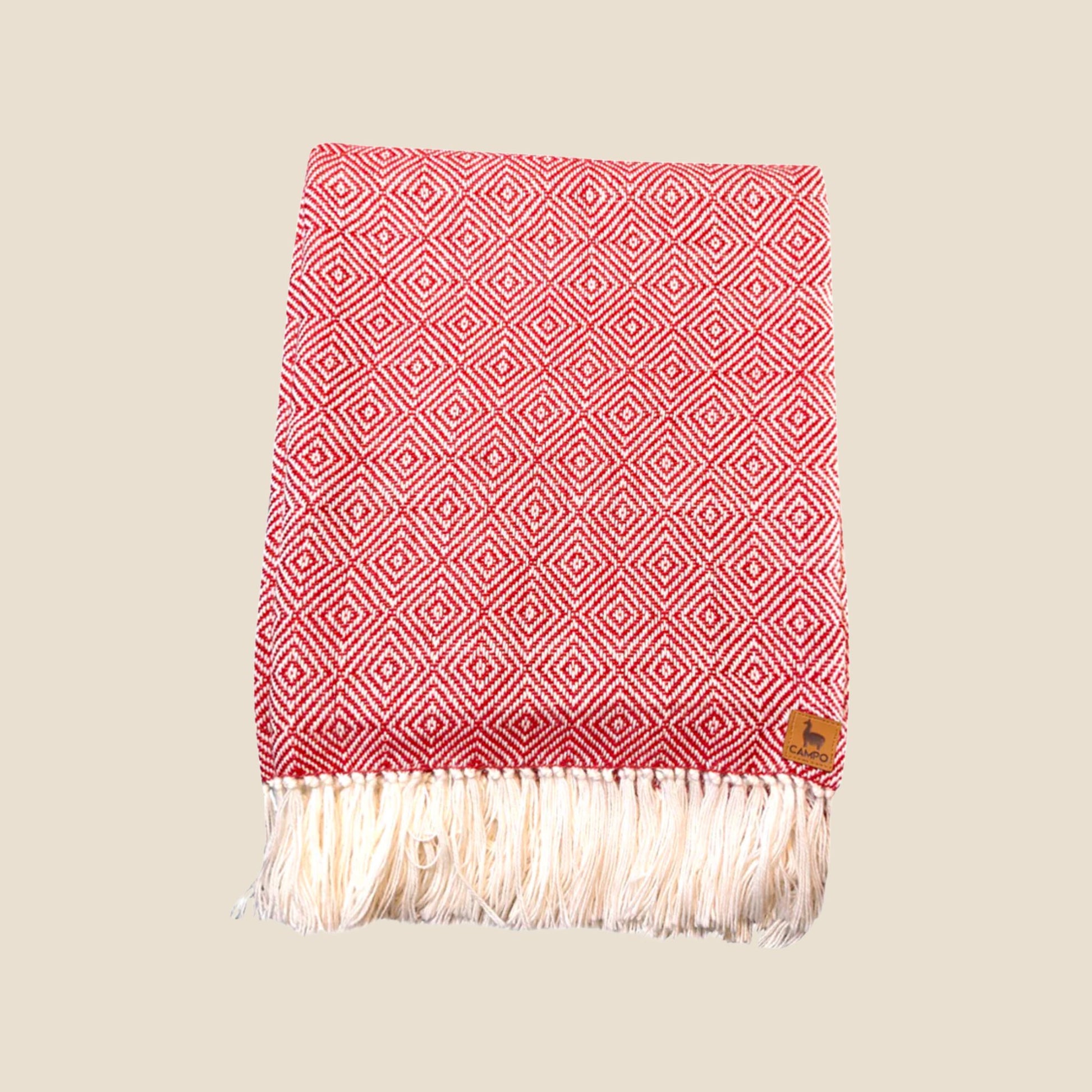 Red and white patterned throw blanket with fringes on a beige background