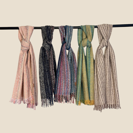 Five scarves of different colors hanging on a rod against a beige background
