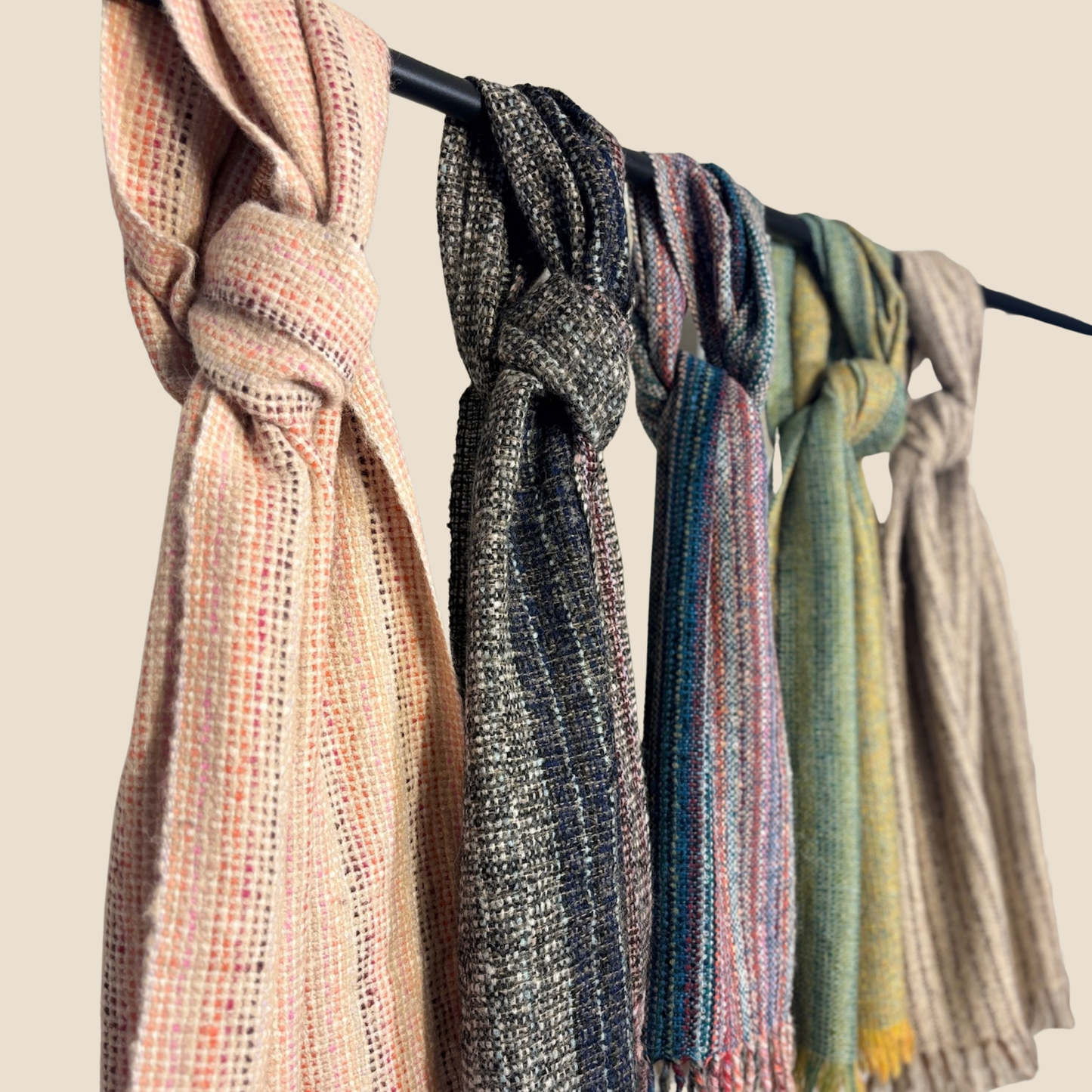 Scarf with various patterns and colors hanging on a rack against a neutral background