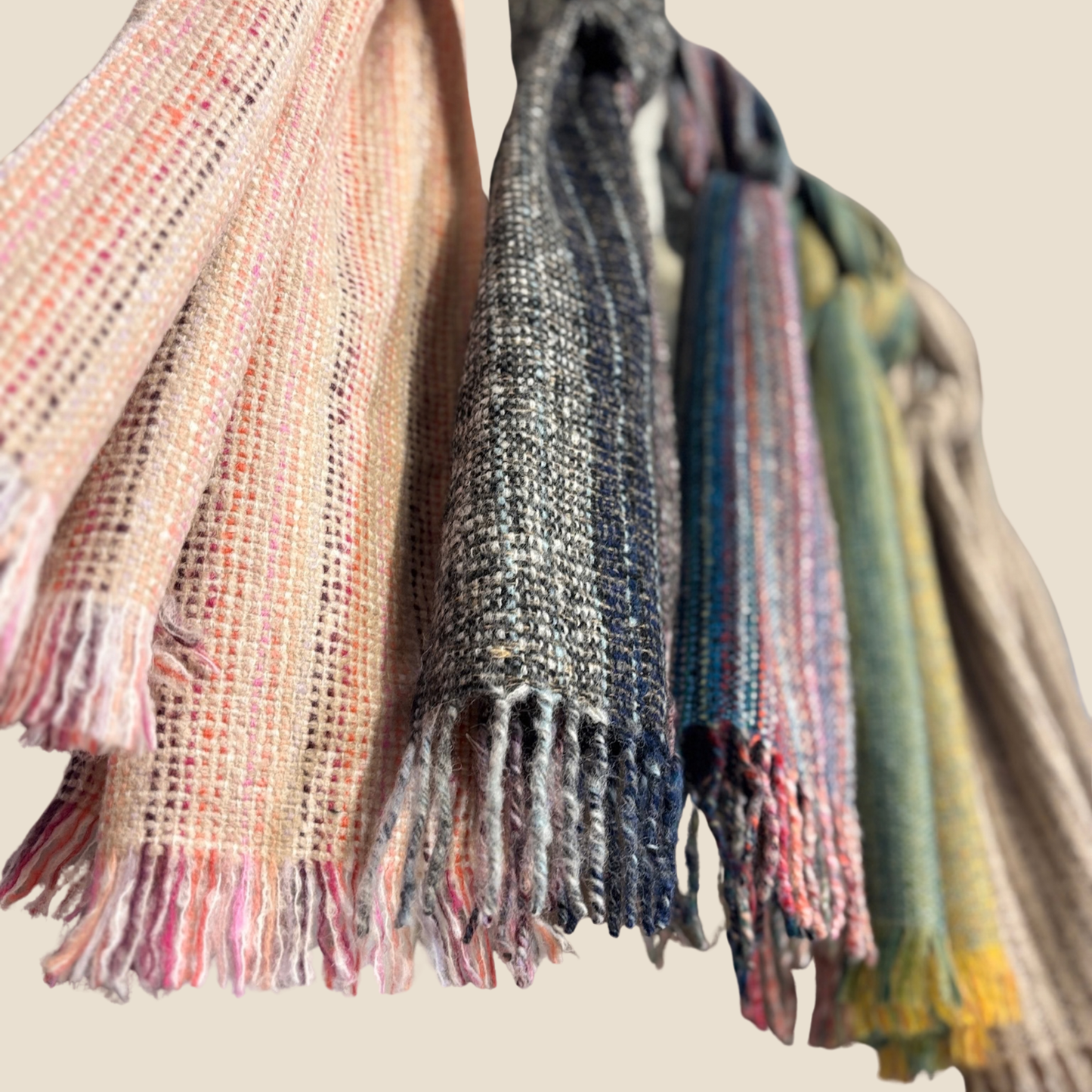 Three scarves with fringe hanging against a neutral background