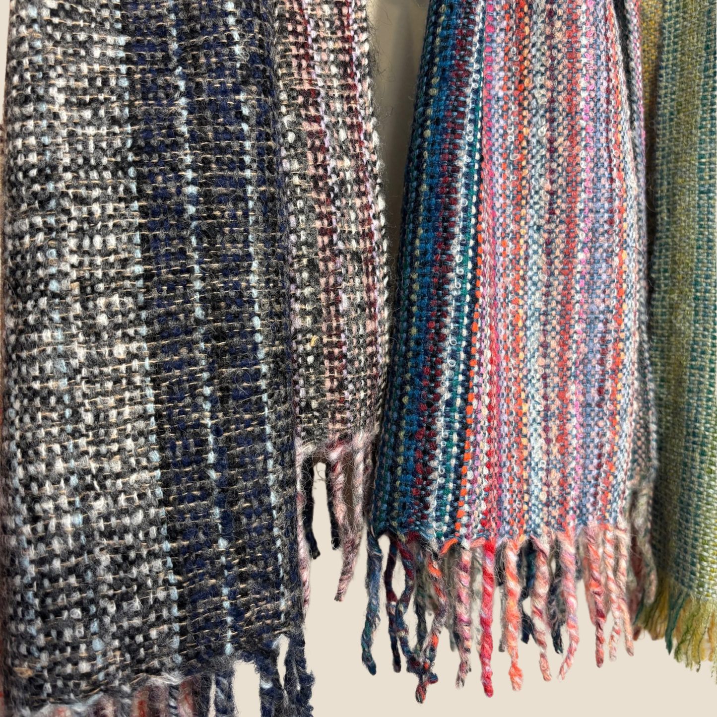 Three woven scarves with different patterns and colors hanging against a neutral background.