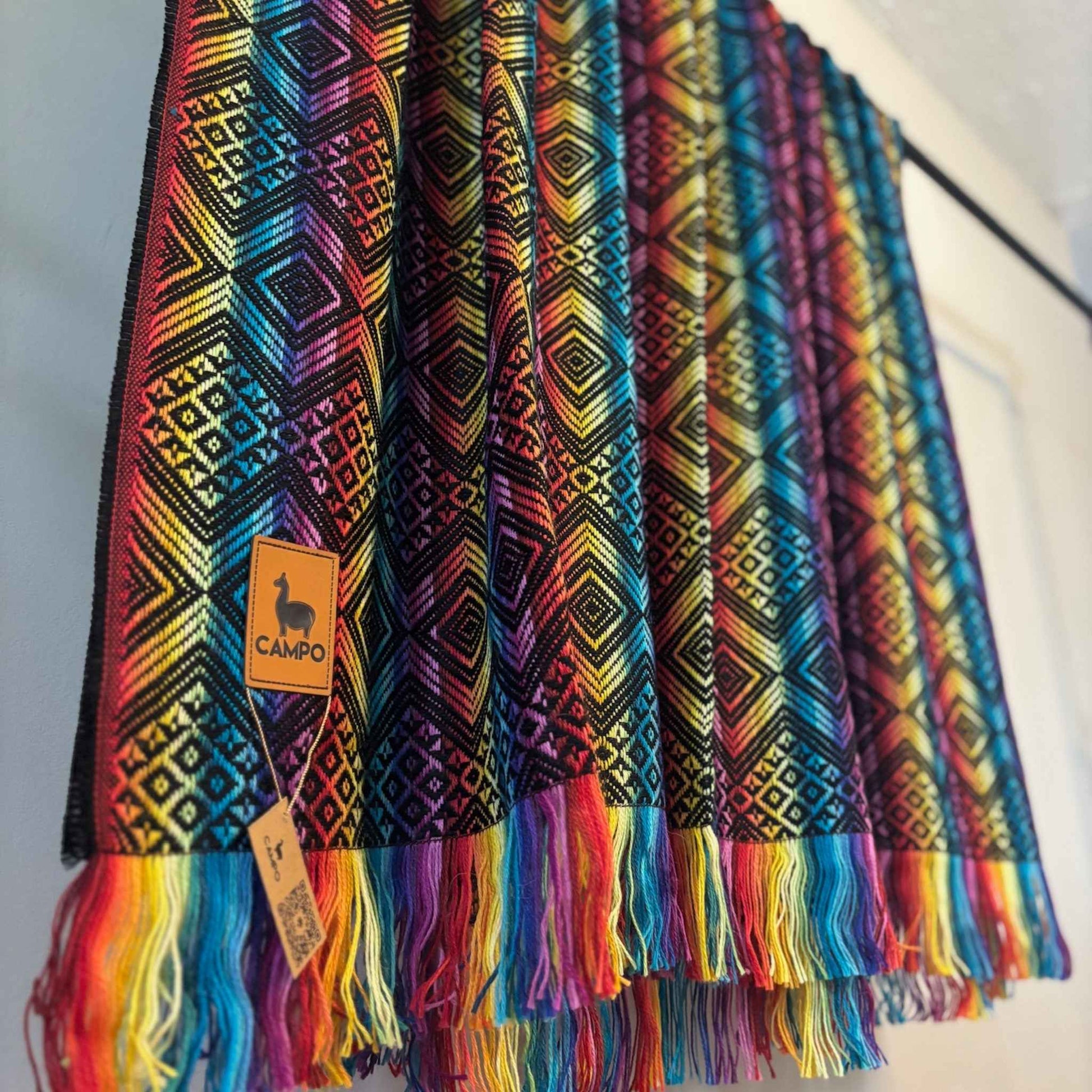 Black rainbow patterned scarf with fringes and a visible brand label on a white background