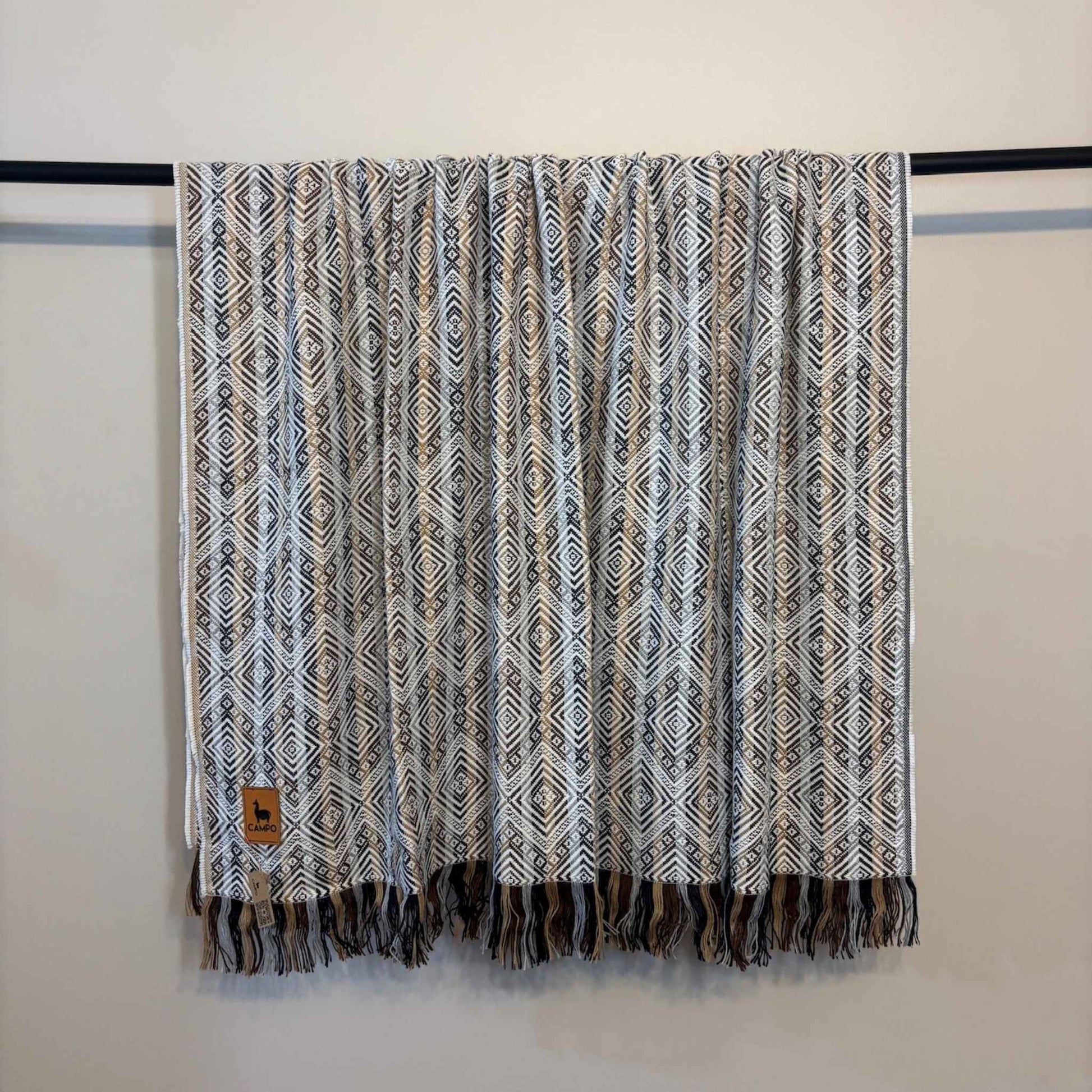 White Natural patterned throw blanket with fringes on a rod against a white wall
